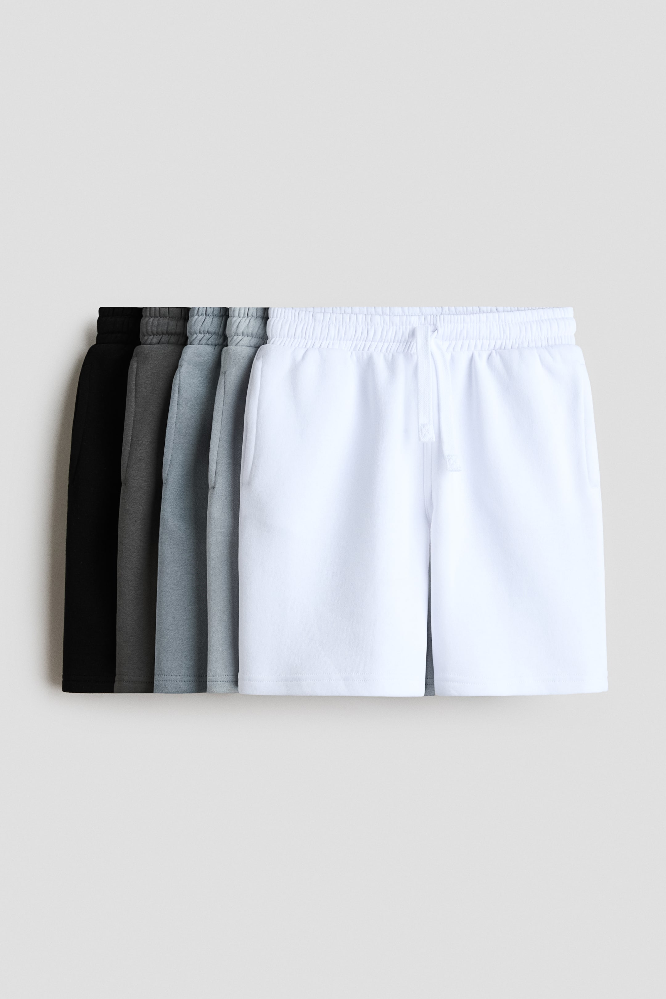 Grösseres Bild ansehen: Knielange Shorts werden von vorne in fünf gestuften Farbvarianten präsentiert: Weiss, Hellgrau, Mittelgrau, Dunkelgrau und Schwarz. Jedes Paar besteht aus einem leichten Sweatshirtstoff, einem elastischen Bund mit Kordelzug und dezenten Seitentaschen.