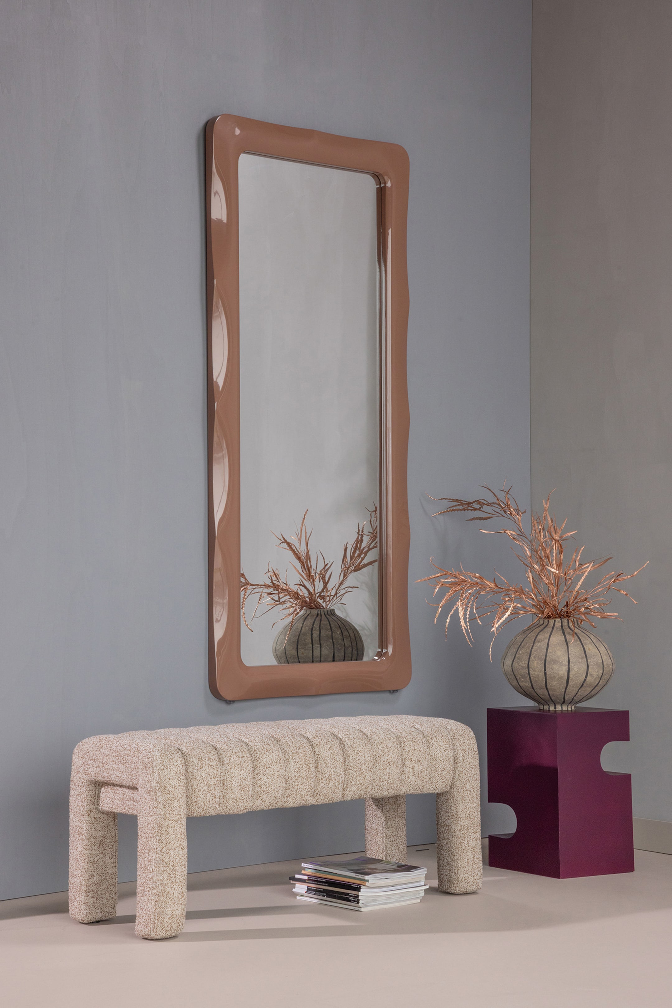 Agrandir l'image: Un miroir pleine longueur avec un cadre brillant de couleur brun clair, doté de bords latéraux ondulés et ondoyants ainsi que de coins arrondis, reflète un vase avec des plantes séchées.