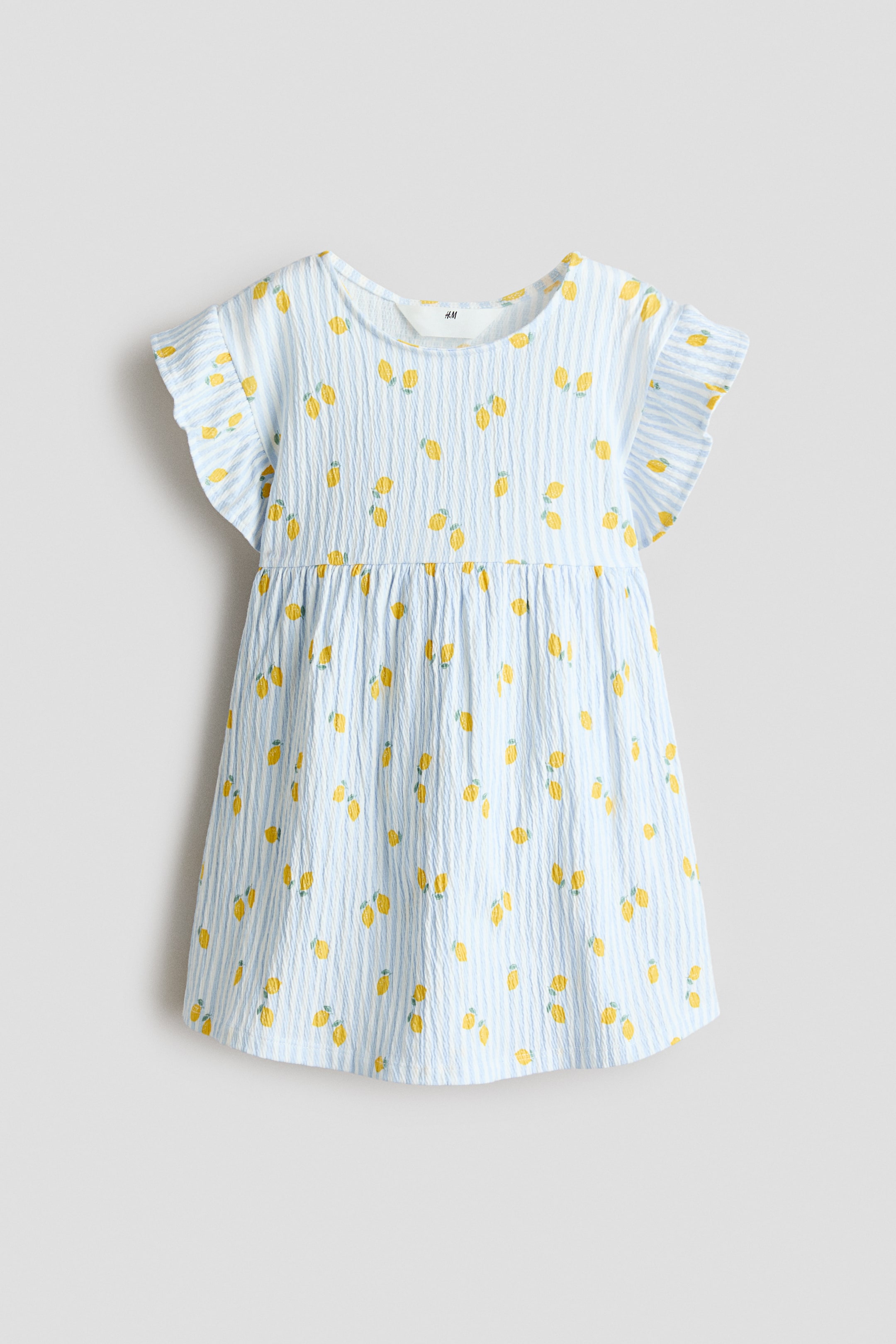Xem ảnh lớn hơn: Váy cotton tay cánh tiên. Chiếc váy, nhìn từ phía trước, nổi bật với chất liệu vải sọc dọc màu xanh nhạt và trắng, có kết cấu với họa tiết chanh vàng rải rác. Váy có tay cánh tiên, cổ tròn và đường may nhún tạo nên một chân váy xòe.