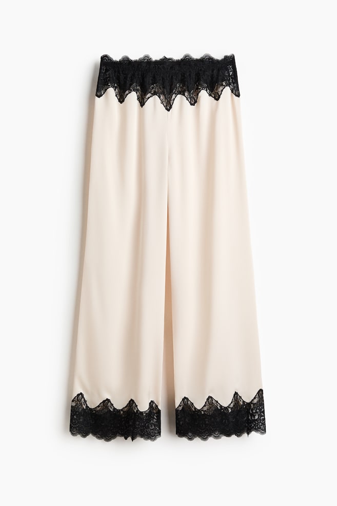 Le pantalon à jambes larges est confectionné dans un tissu beige clair et est orné de dentelle noire festonnée le long de la ceinture et des ourlets inférieurs. - 1