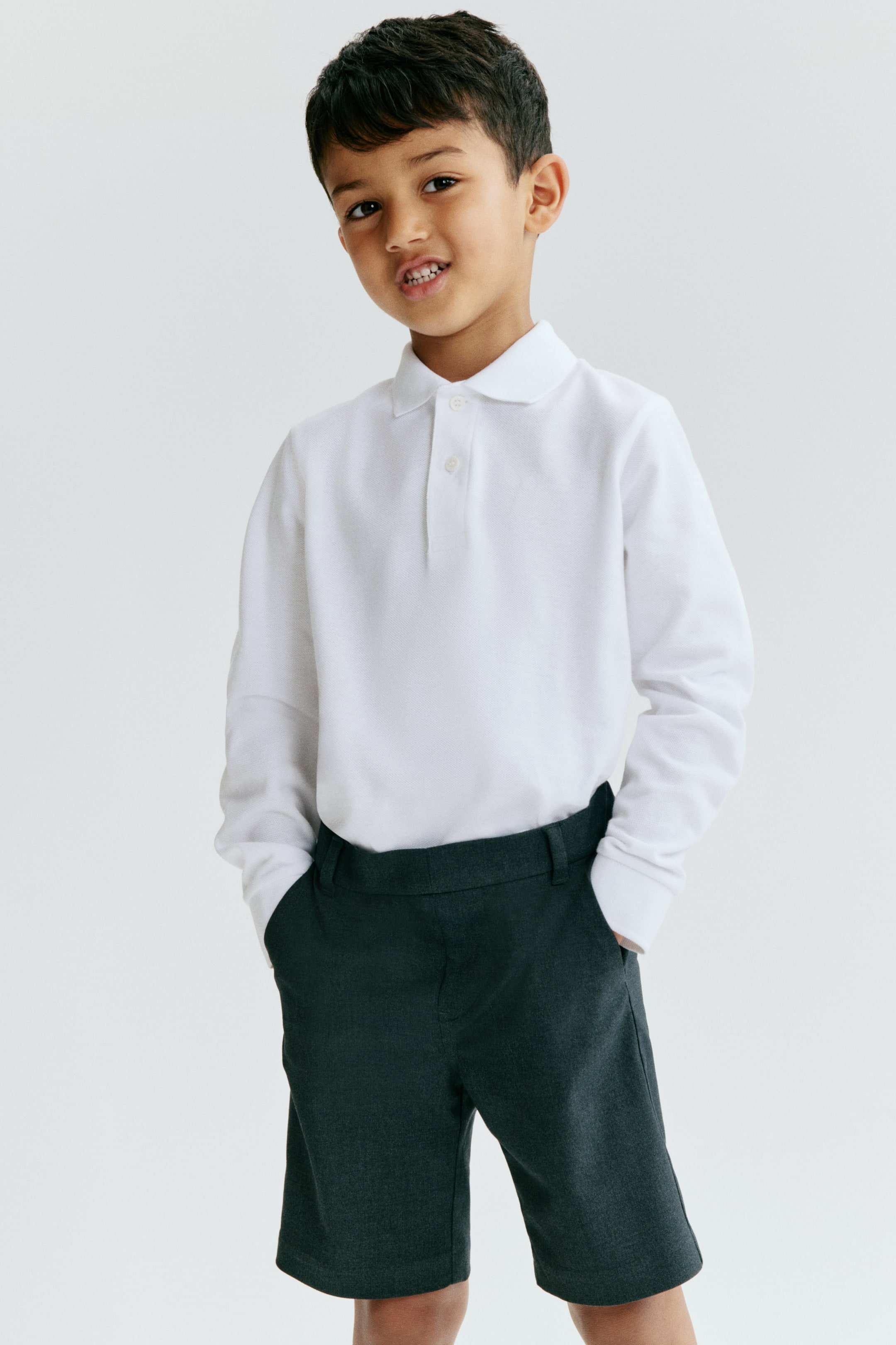 View larger image: A white long-sleeved school polo shirt is displayed from the front, highlighting a pique knit texture. It features a classic collar and a two-button placket, with the long sleeves finishing in ribbed cuffs.