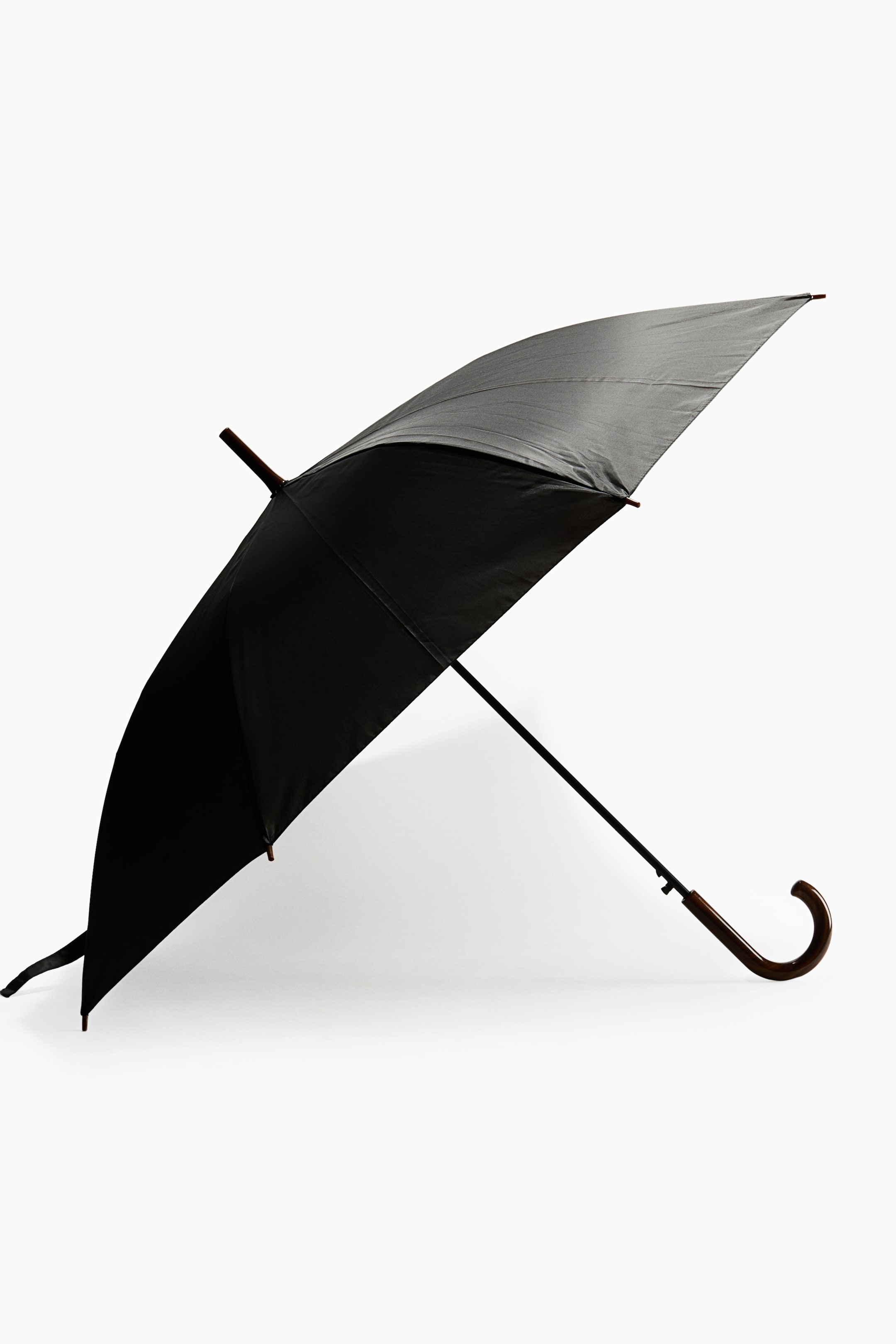 Vezi imaginea mai mare: O umbrelă neagră deschisă este așezată pe o parte, evidențiindu-și pânza neagră a cupolei, tija metalică neagră și mânerul curbat din lemn, în formă de J. Umbrela pune în valoare vârfurile din lemn de la capetele spițelor și o ferulă din lemn asortată în partea de sus.