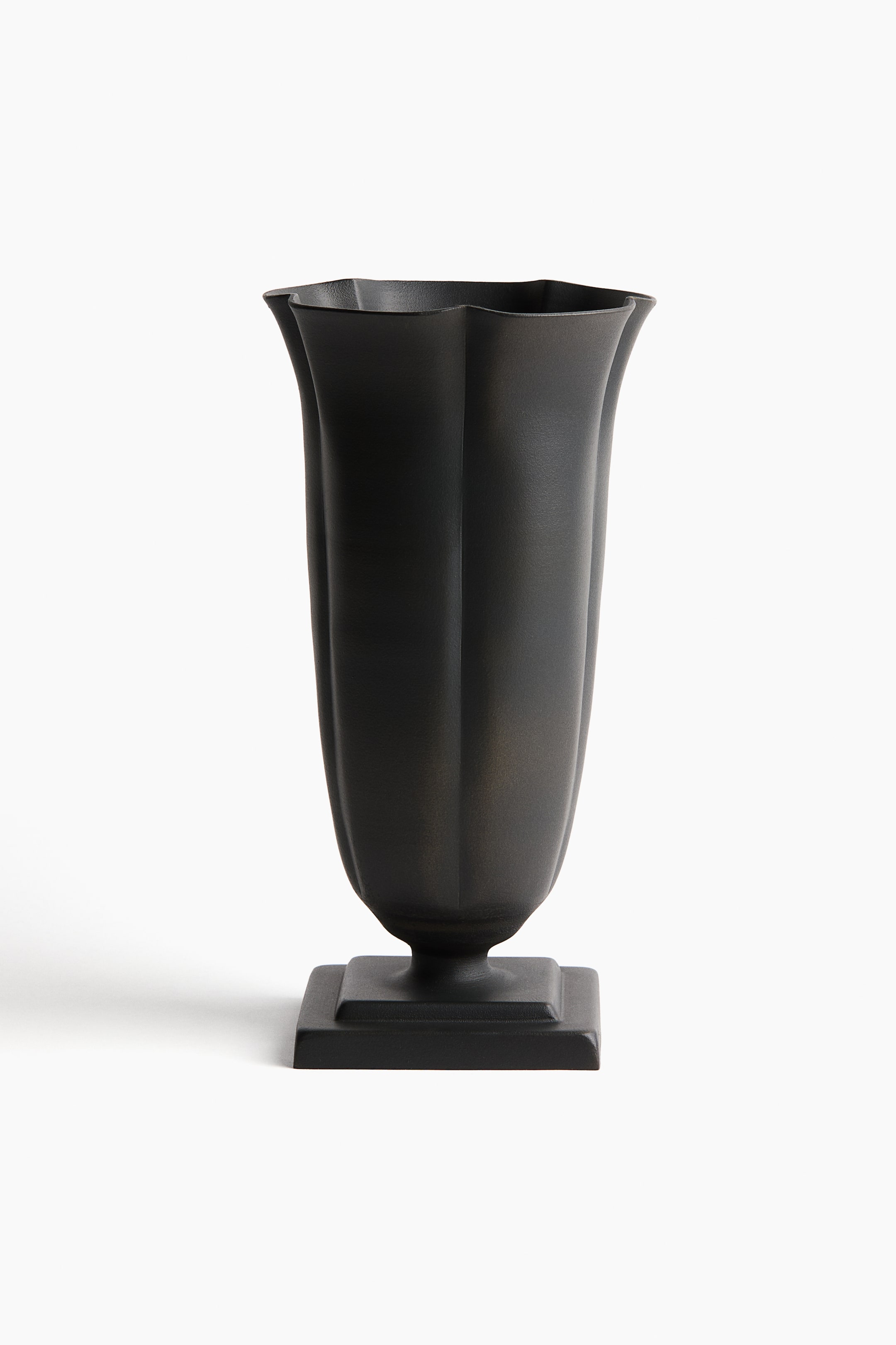 View larger image: A dark, matte vase is standing front-facing, displaying a scalloped rim and a faceted, tapering body. It is resting on a square plinth base.