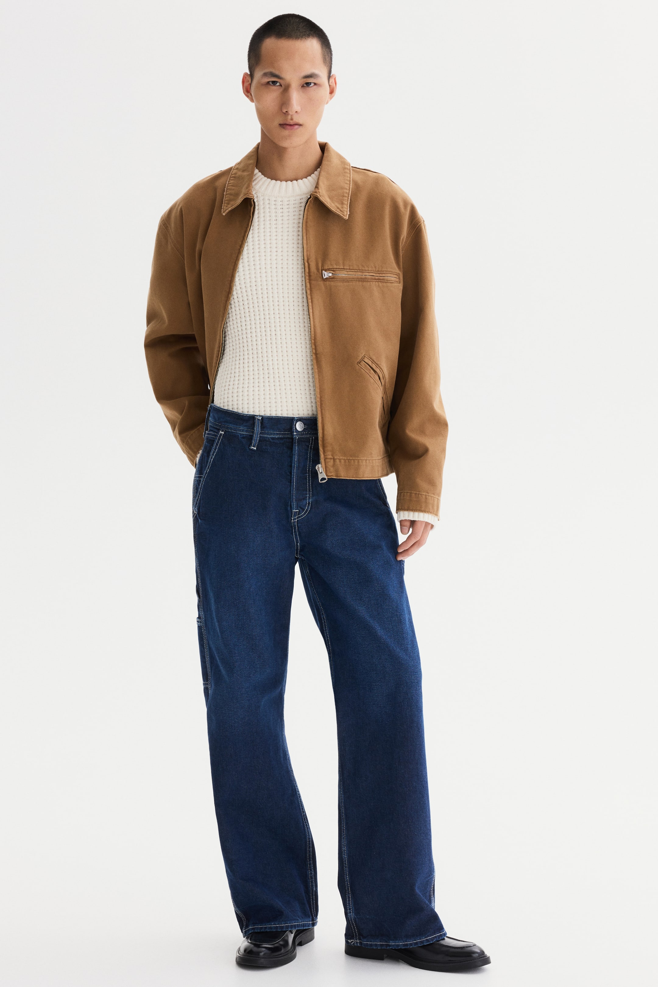 View larger image: A brown workwear-style jacket with a collared neckline, a zip chest pocket and a front zip fastening is worn over a cream waffle-knit crew neck sweater and dark blue wide-leg carpenter jeans, detailed with contrast stitching and a side utility pocket.