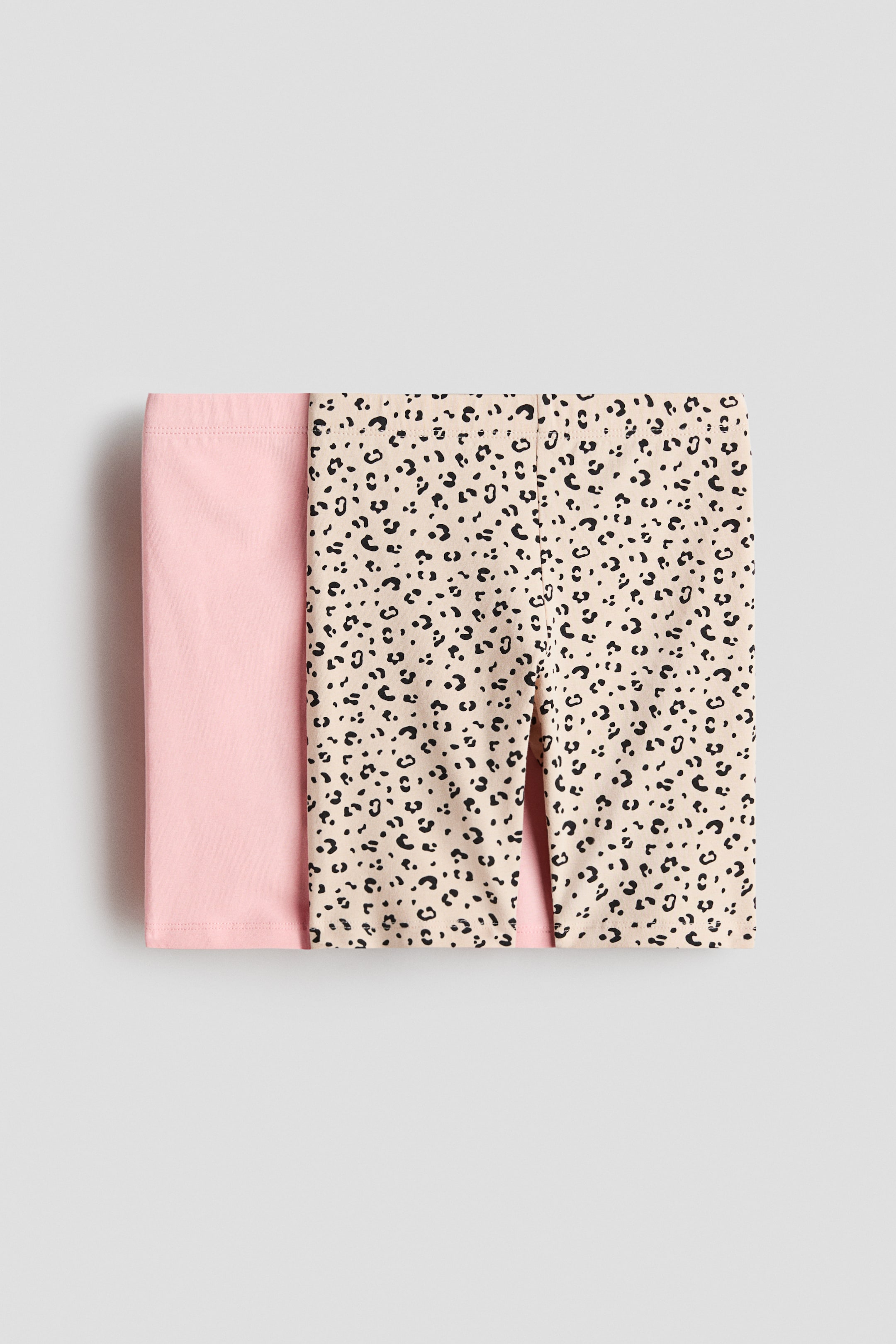 View larger image: Two pairs of cycling shorts crafted from soft cotton jersey with an elastic waistband are displayed in a neatly folded stack. One pair comes in a solid light pink, while the other features a beige base with a black leopard print.