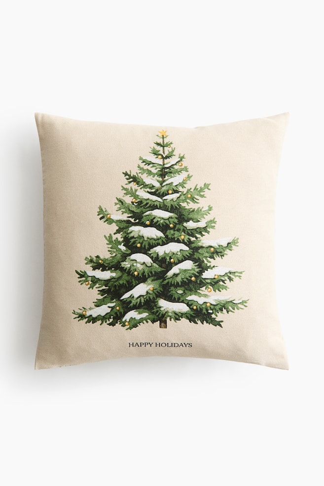 Een vierkant sierkussen van lichtbeige geweven stof toont een frontale illustratie van een groene groenblijvende boom, versierd met witte sneeuw, kleine gouden ornamenten en een gele ster als top. De tekst "HAPPY HOLIDAYS" staat in zwarte hoofdletters direct gecentreerd onder de boomafbeelding. - 1