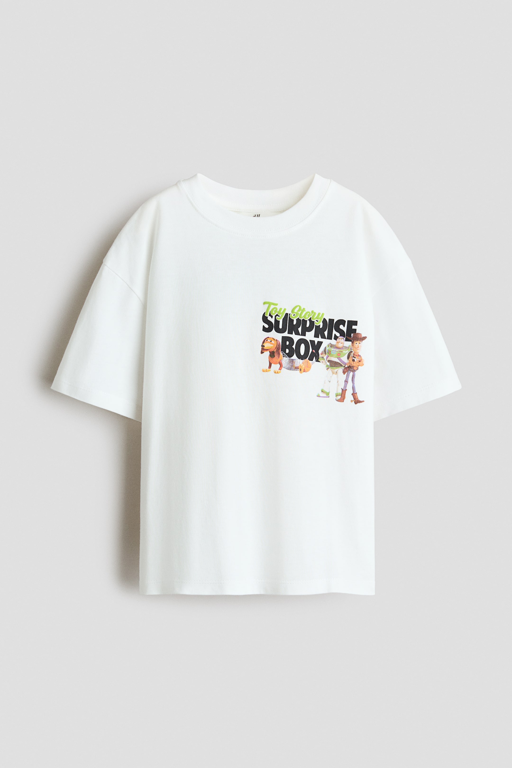 Grösseres Bild ansehen: Ein weisses, locker sitzendes T-Shirt ist von vorne zu sehen, mit einem runden, gerippten Ausschnitt und überschnittenen Schultern. Es zeigt einen bunten "Toy Story Surprise Box"-Druck mit Charakteren auf der linken Brust.