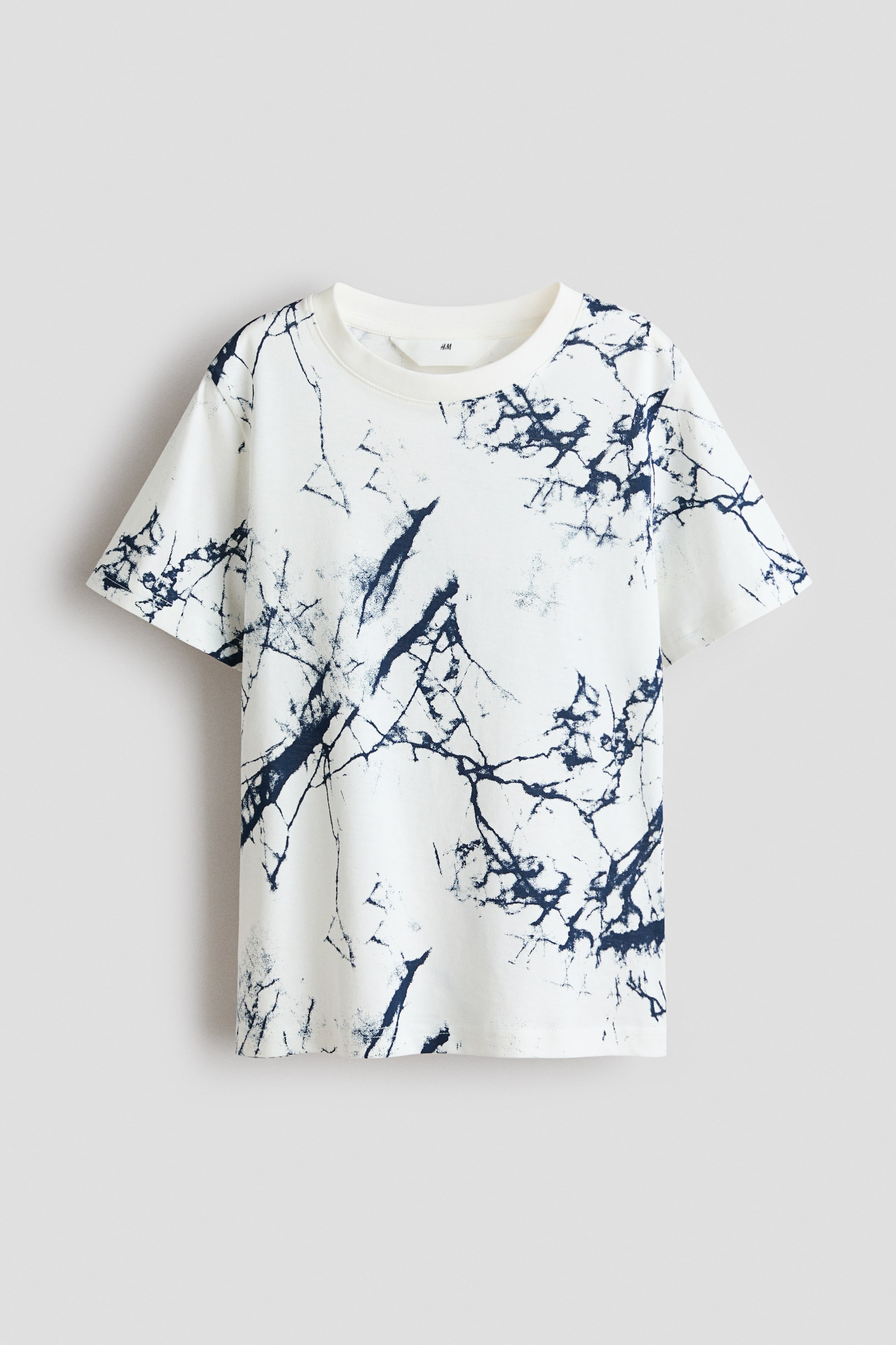 View larger image: A front view of a white T-shirt in printed cotton jersey. It features an all-over dark-blue abstract, marble-like pattern and is designed with short sleeves and a ribbed, round neckline.