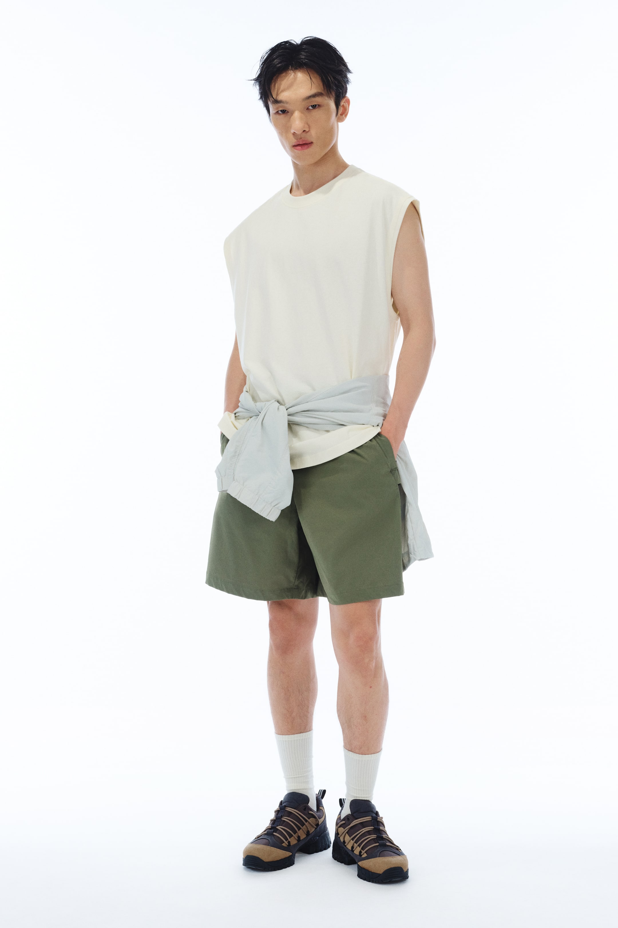 View larger image: A cream cotton jersey vest top, featuring a round, rib-trimmed neckline, armholes with raw edges, and a straight-cut hem, is being worn by the model. The loose-fitting top is styled with a light blue shirt being tied around the model's waist.