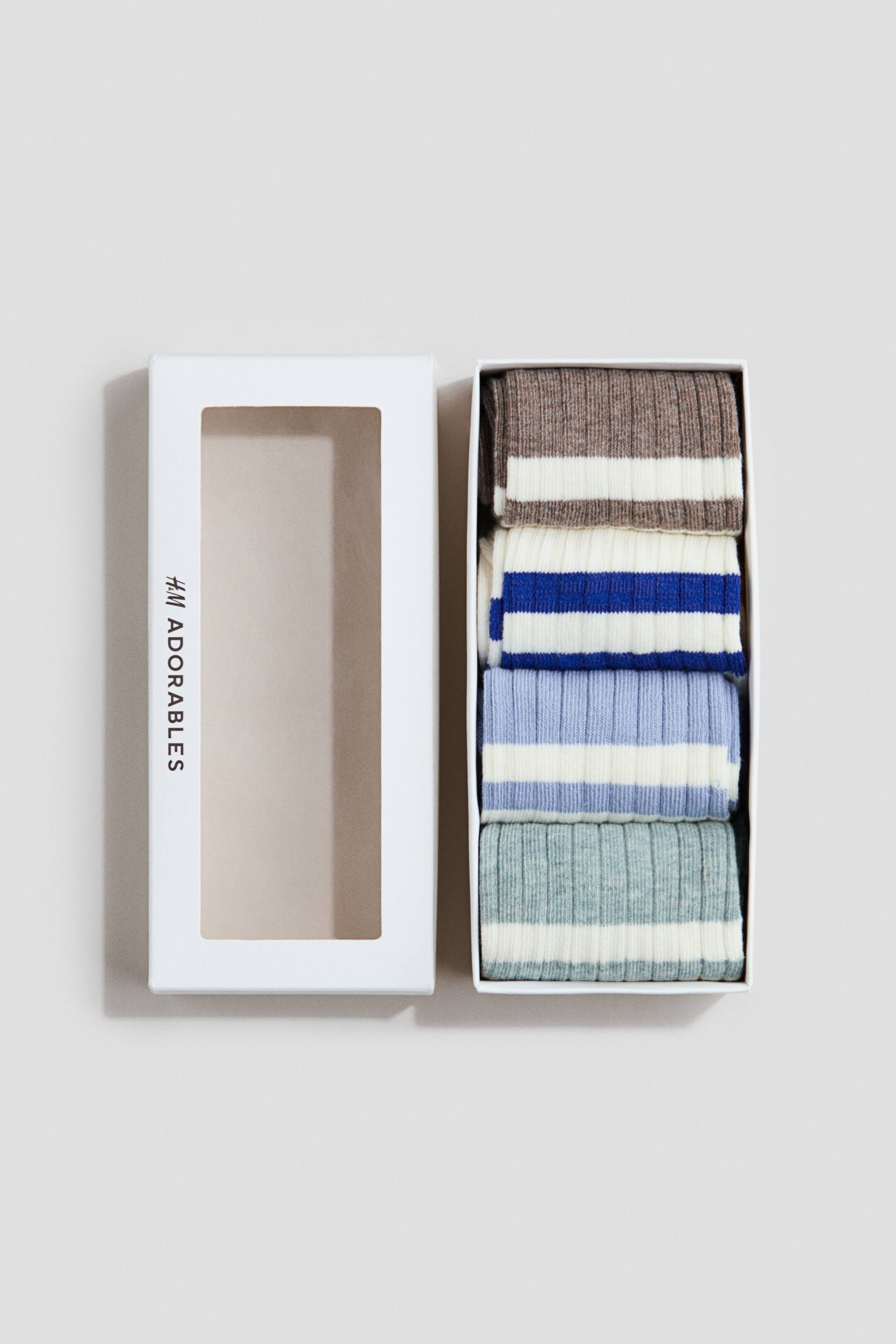 Grösseres Bild ansehen: H&M Adorables Rippenstrick-Socken werden in einer weissen rechteckigen Box mit offenem Fenster präsentiert. Vier Paar gefaltete, gestreifte Socken sind sichtbar, jede mit einer gerippten Textur, darunter braun mit einem weissen Streifen, weiss mit einem königsblauen Streifen, hellblau mit einem weissen Streifen und hellgrün mit einem weissen Streifen.