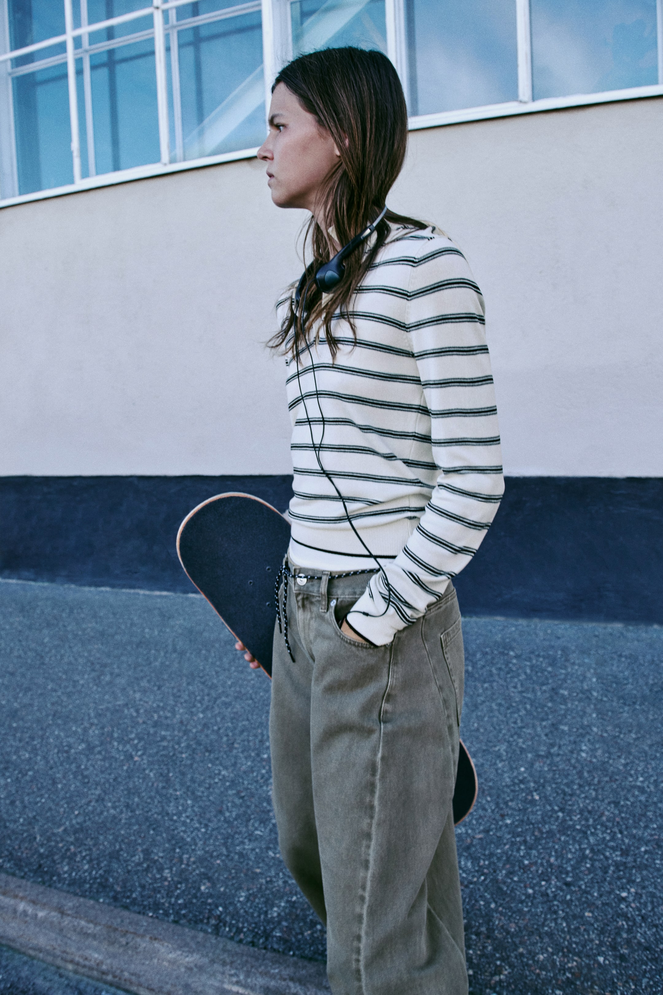 View larger image: A long-sleeved polo shirt in a fine-knit viscose blend, featuring horizontal black and off-white stripes, is shown from a side-profile angle. The shirt is styled tucked into olive green trousers, highlighting its slim fit and ribbed cuffs.