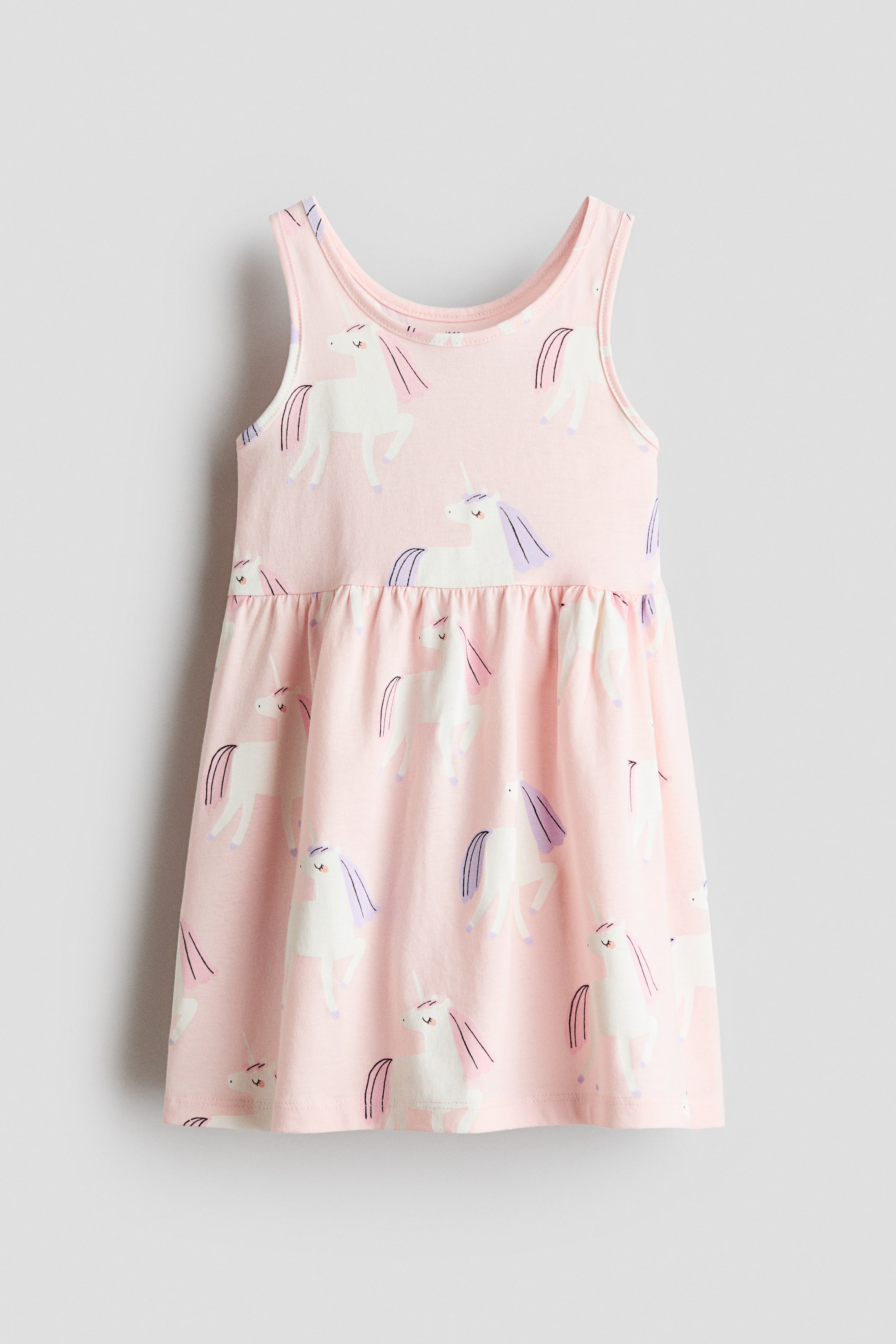 Größeres Bild ansehen: Ein ärmelloses Kleid aus weichem, rosa Jersey zeigt sich von vorne und präsentiert ein Muster aus weißen Einhörnern. Eine geraffte Naht ist an der Taille sichtbar, die zu einem sanft ausgestellten Rock führt.