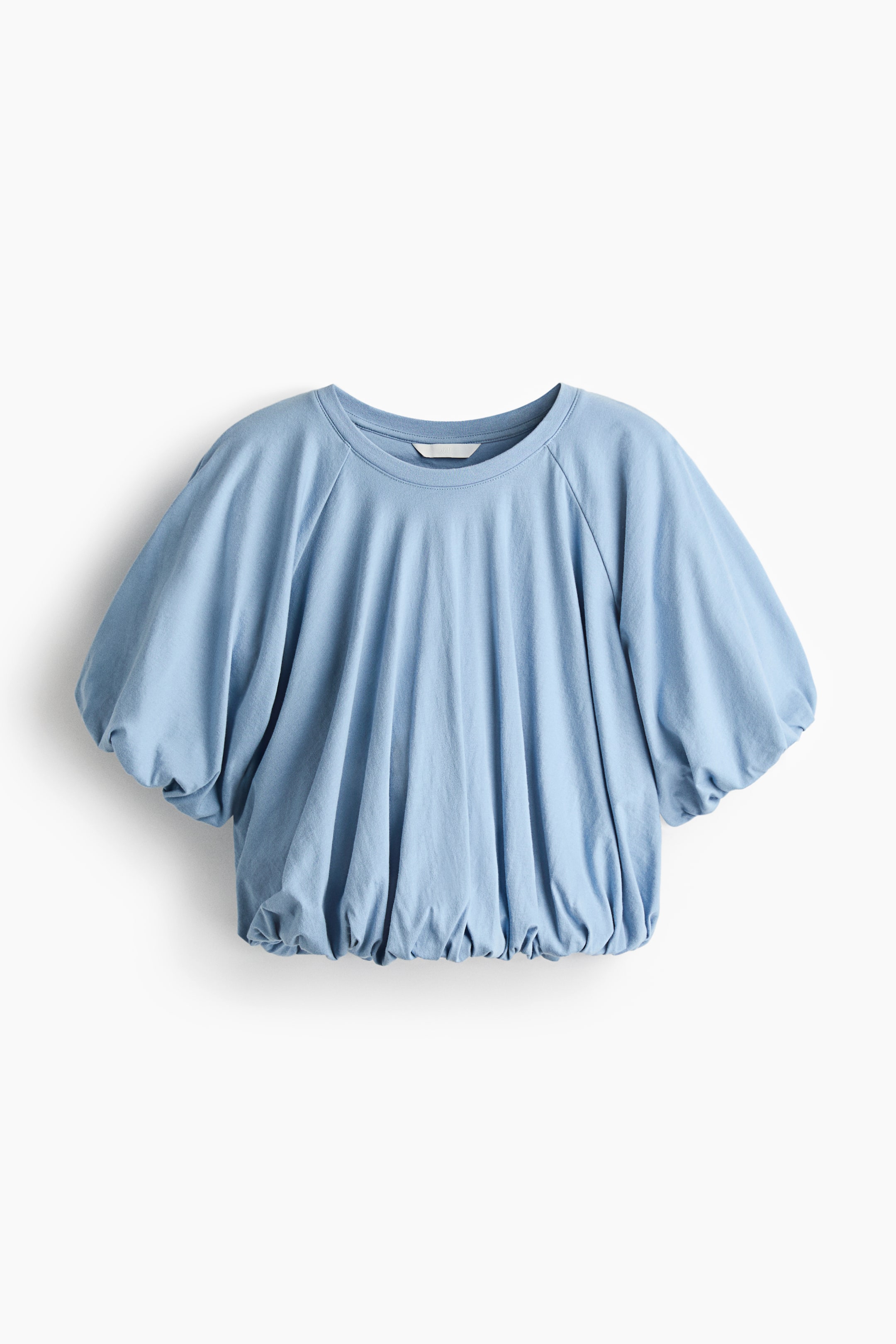 View larger image: A light-blue top is shown from the front, featuring a crew neck and voluminous raglan sleeves gathered above the elbow. The body of the top is loosely fitted, with the hem gathered to create a blouson effect.