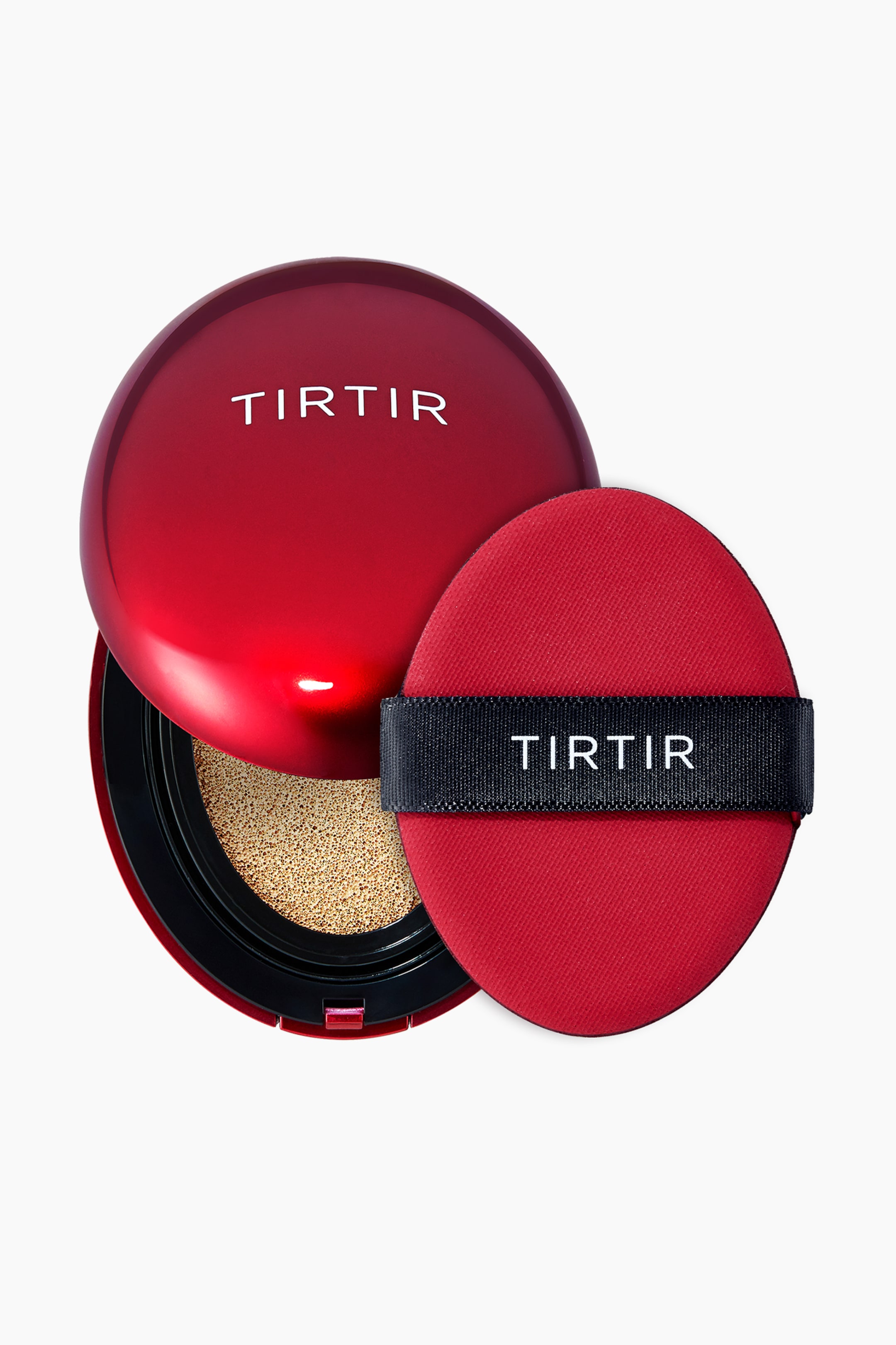 Vis større bilde: En blank, rød Tirtir cushion compact er åpen, og viser en beige foundation-dyppet pute innenfor sin svarte base, mens en rød oval sminkepuff med en svart "TIRTIR" stropp hviler ved siden av.