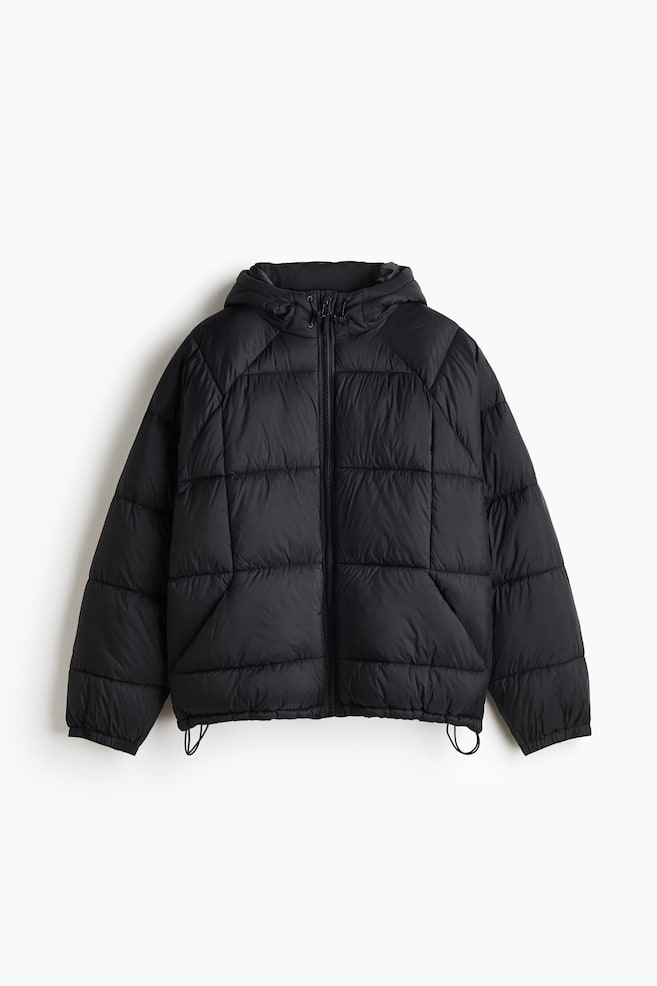A black puffer jacket is shown from the front, featuring rectangular quilted panels and a full-length central zipper. It includes an attached hood with adjustable drawstrings, elasticated cuffs, and a straight hem with hanging drawcords. - 1