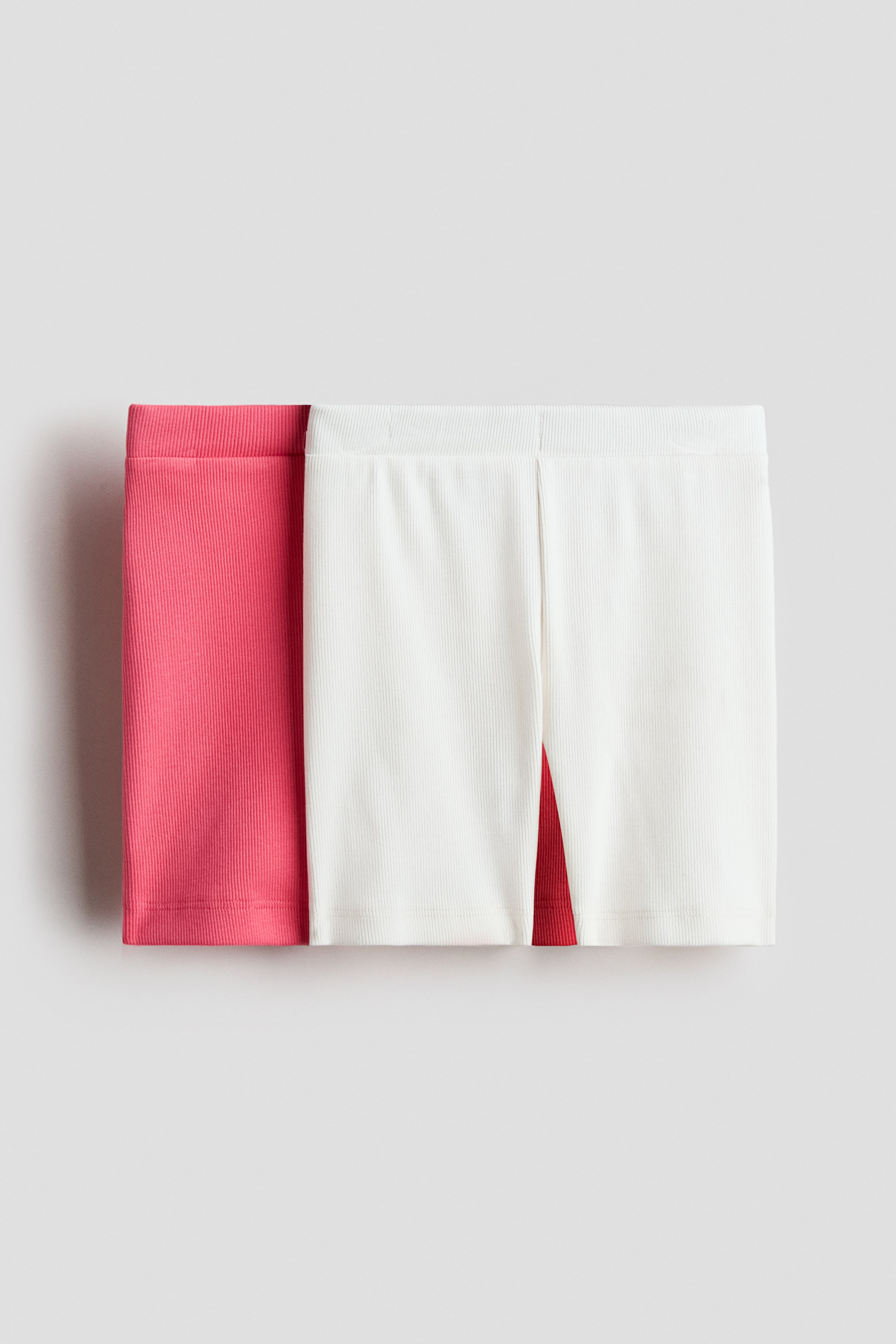 View larger image: Two pairs of ribbed jersey cycling shorts are shown, highlighting their front. One pair is a vibrant coral pink, while the other is off-white, both featuring an elastic waistband.