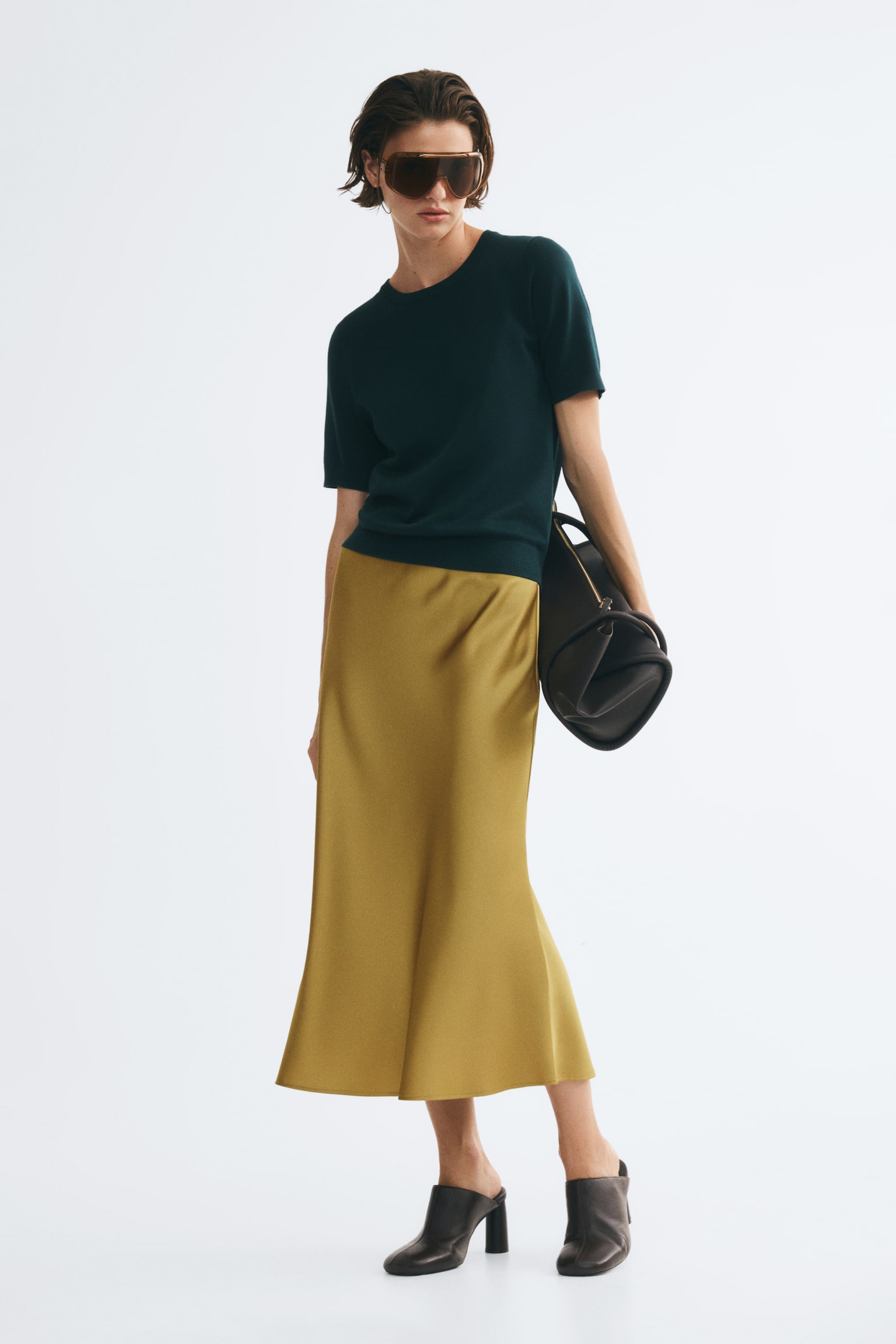 A gold calf-length skirt is displayed from the front, featuring a softly draping weave with a slight sheen, a high waist, and a gentle flare to the hem. - 1