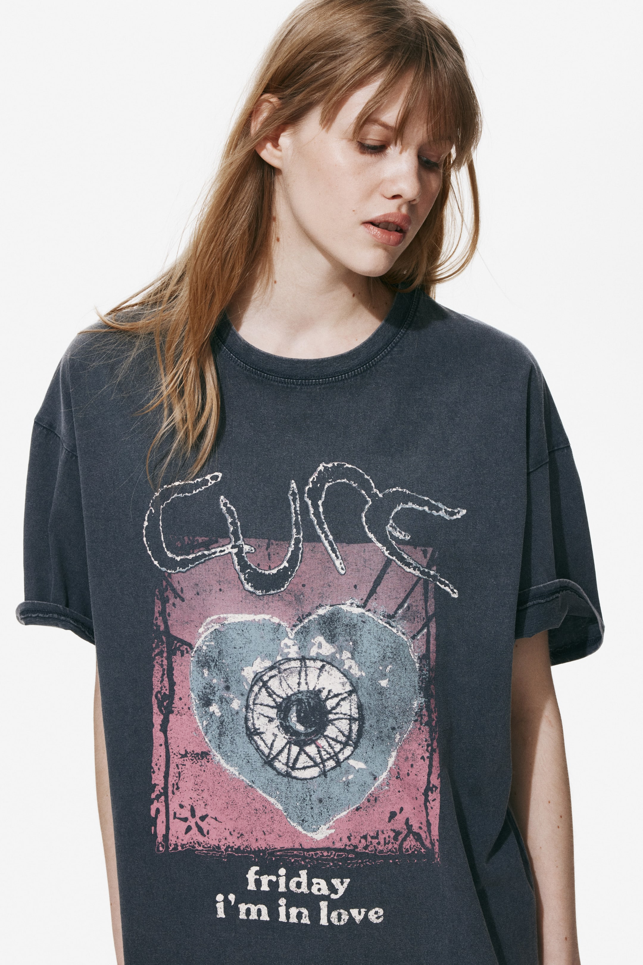 View larger image: The dark gray, faded t-shirt features a distressed graphic on the front, showcasing "CURE" text, a pink and blue heart with a central eye, and "Friday I'm in Love" text. It is designed with a crew neck and rolled short sleeves.