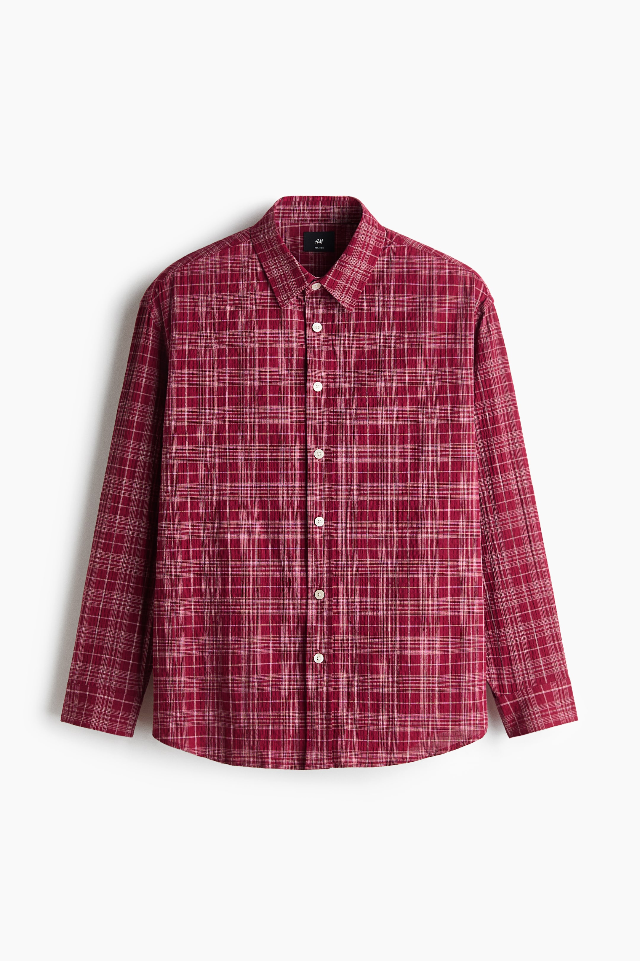 View larger image: A long-sleeved cotton seersucker shirt in a red and white plaid pattern is shown from the front, with a relaxed silhouette. It features a classic collar, a button-down front with white buttons, and a gently rounded hem.