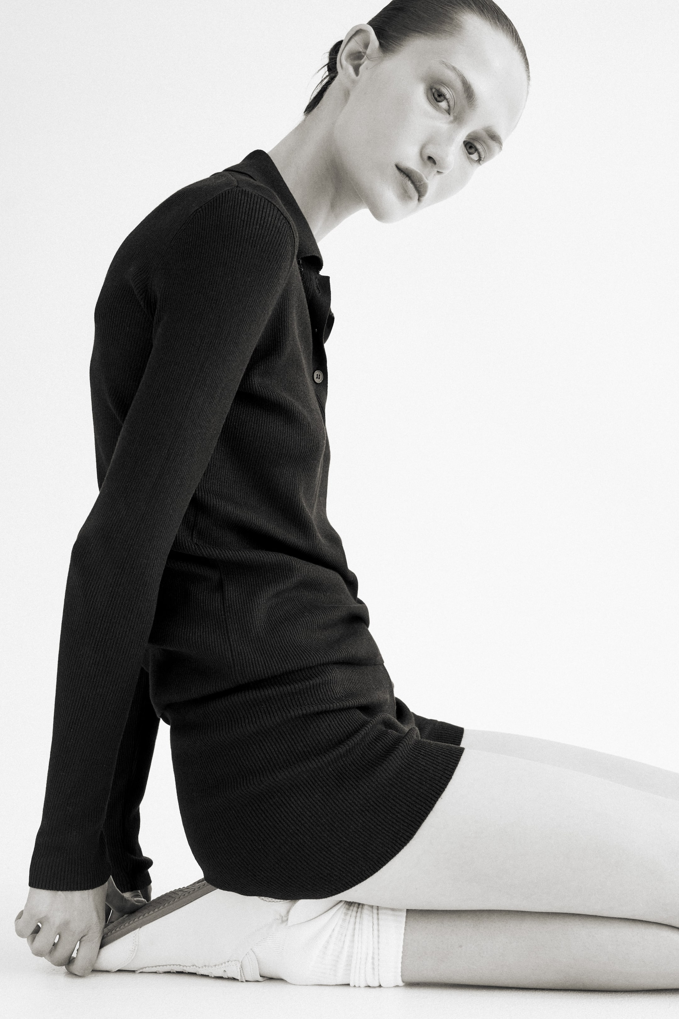 Visualizza immagine più grande: Pantaloncini aderenti in tessuto a coste nero indossati dalla modella. I pantaloncini sono abbinati a un top a maniche lunghe nero a coste, con un indumento bianco visibile sotto i pantaloncini.
