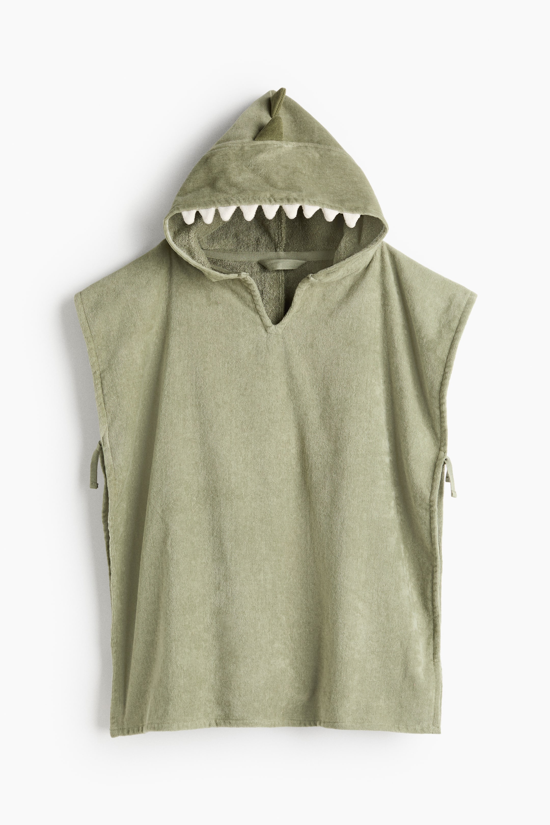 拡大画像を表示: 緑のタオルケープが正面からクリーチャー風のフードを見せており、フード上部にはやわらかな三角形の突起が並び、フードの開口部にはギザギザした白い歯があしらわれています。ケープはVネックで、両側に結び紐が付いています。