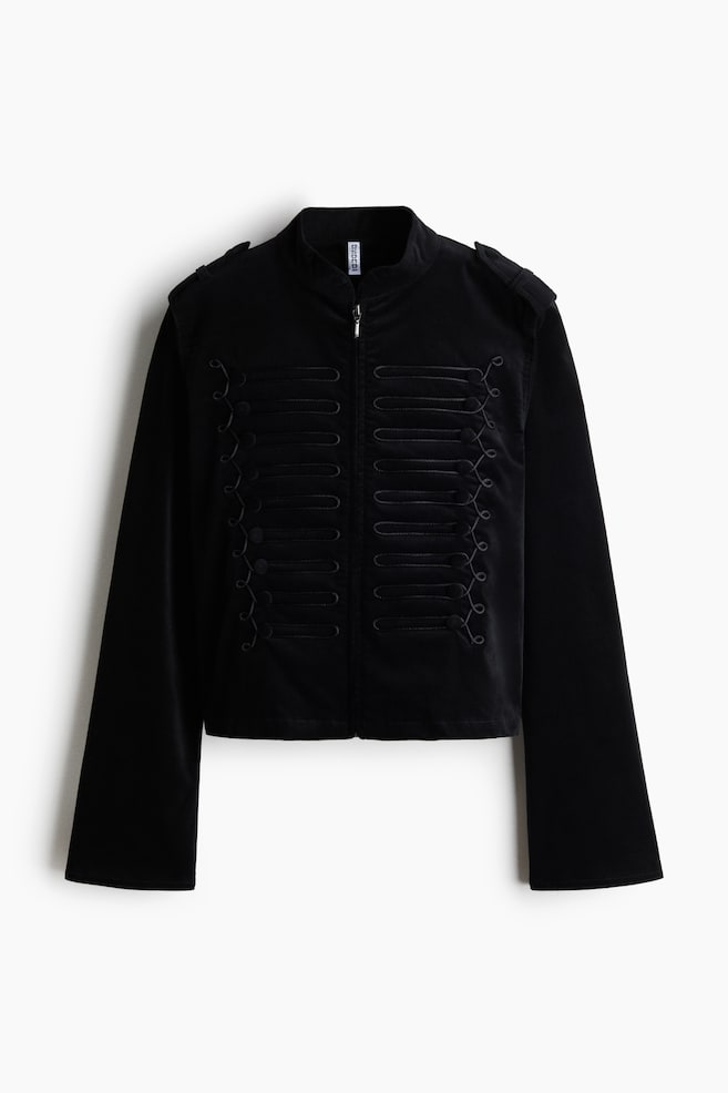 Een zwart jasje in militaire stijl is van voren afgebeeld en heeft een opstaande kraag, schouderepauletten en een ritssluiting vooraan. Symmetrische rijen zwarte decoratieve koordversieringen sieren beide kanten van de borst, terwijl de lange mouwen licht uitlopen naar de manchetten. - 1