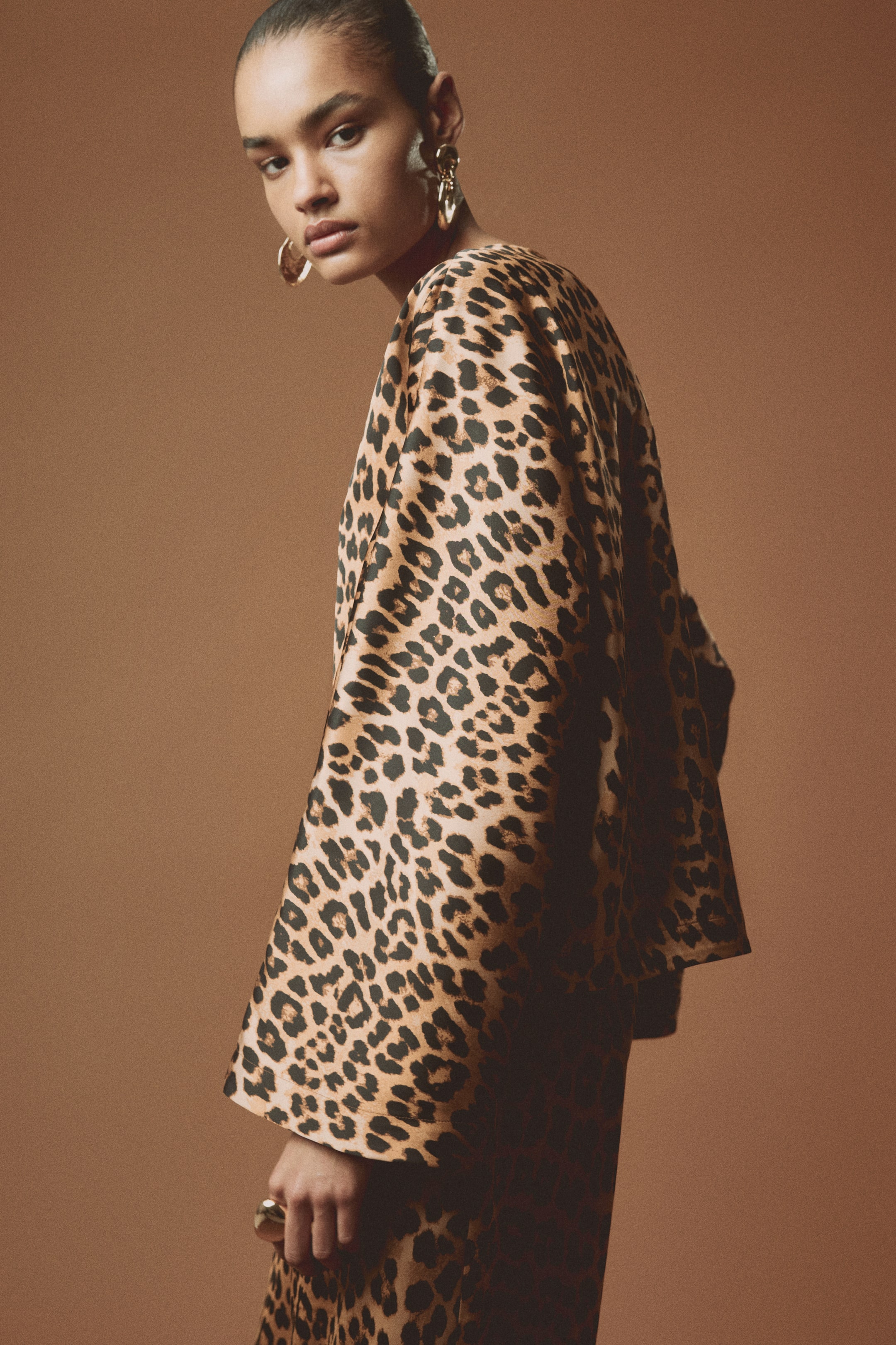 View larger image: A leopard print top showcases a relaxed fit and wide, flowing sleeves, with the garment elegantly draping over the wearer's shoulder and arm from a partial side view. A hand adorned with a large gold-toned ring emerges from the bottom of the sleeve.