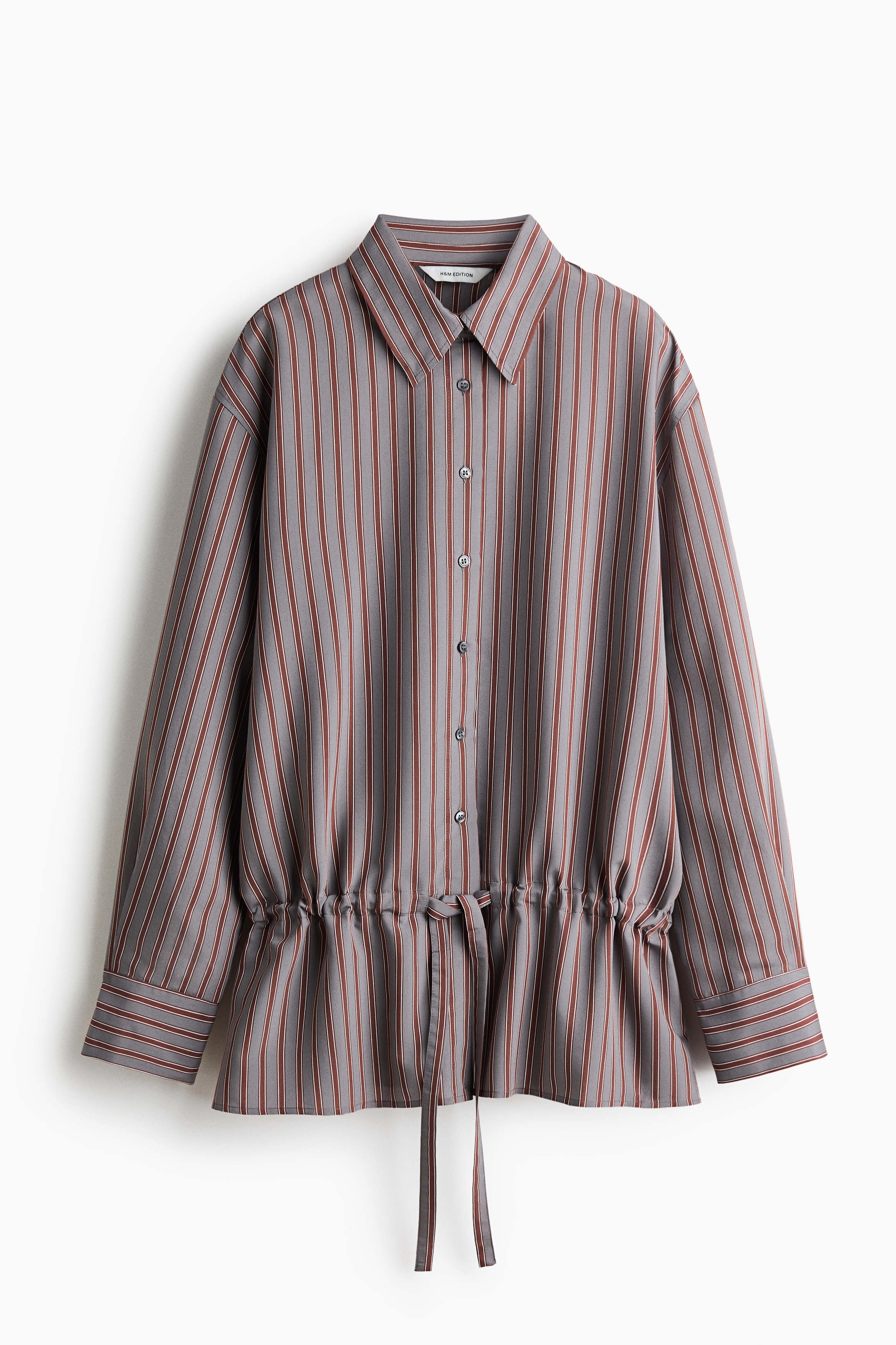 A striped long-sleeved shirt featuring vertical grey and brown stripes is being worn by the model. The shirt is styled with an open collar and is paired with matching striped trousers.