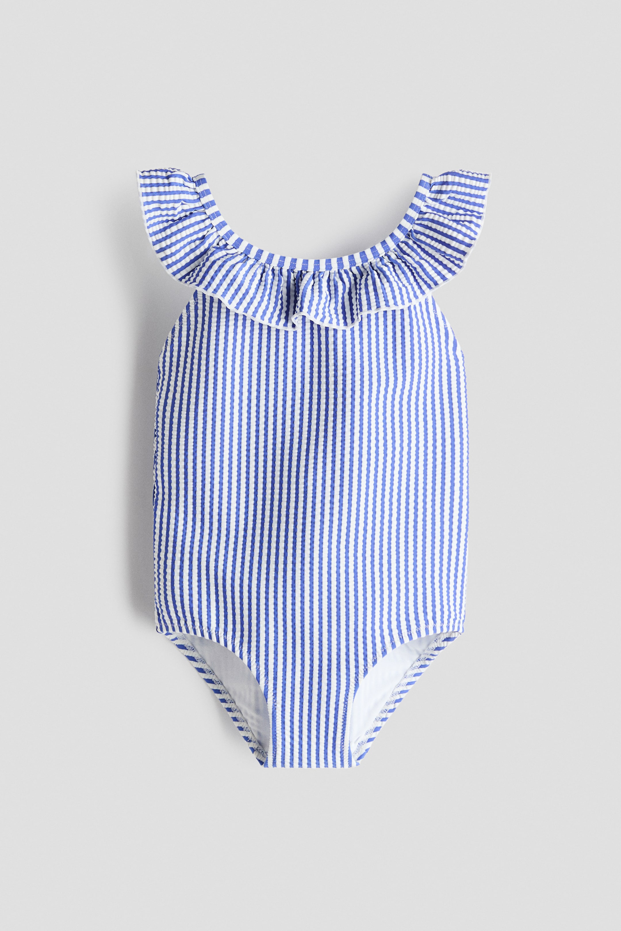 View larger image: A one-piece swimsuit is showcasing its front, featuring blue and white vertical stripes with a seersucker texture. It is designed with a ruffled trim along the neckline, accented by white piping.
