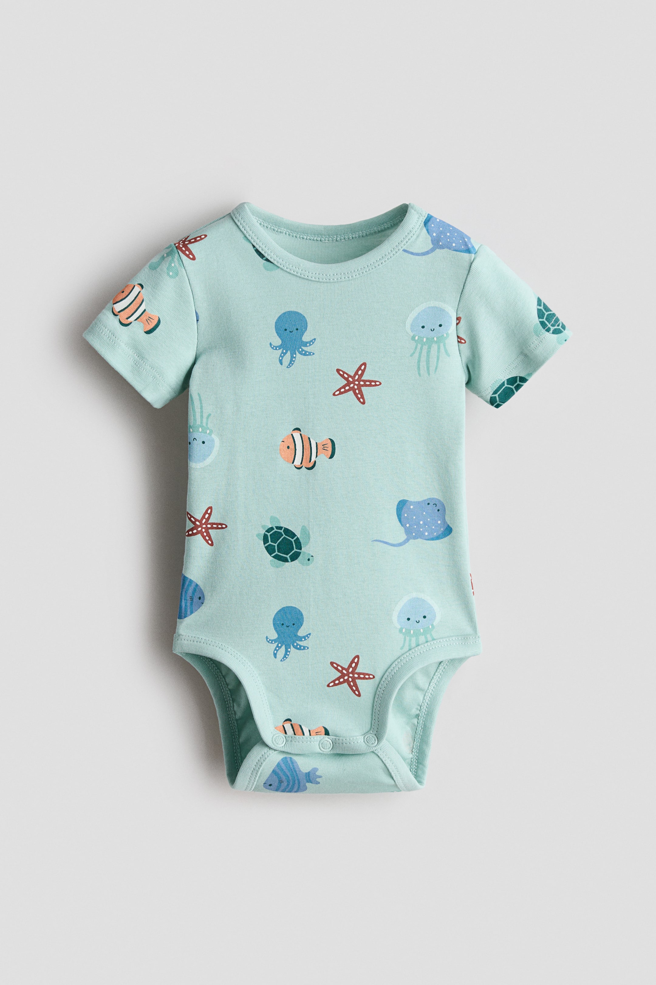 View larger image: A front-facing short-sleeved bodysuit in light blue-green cotton jersey showcases an all-over print of vibrant cartoon sea creatures. It features a round, trimmed neckline, and press-studs secure the bottom.