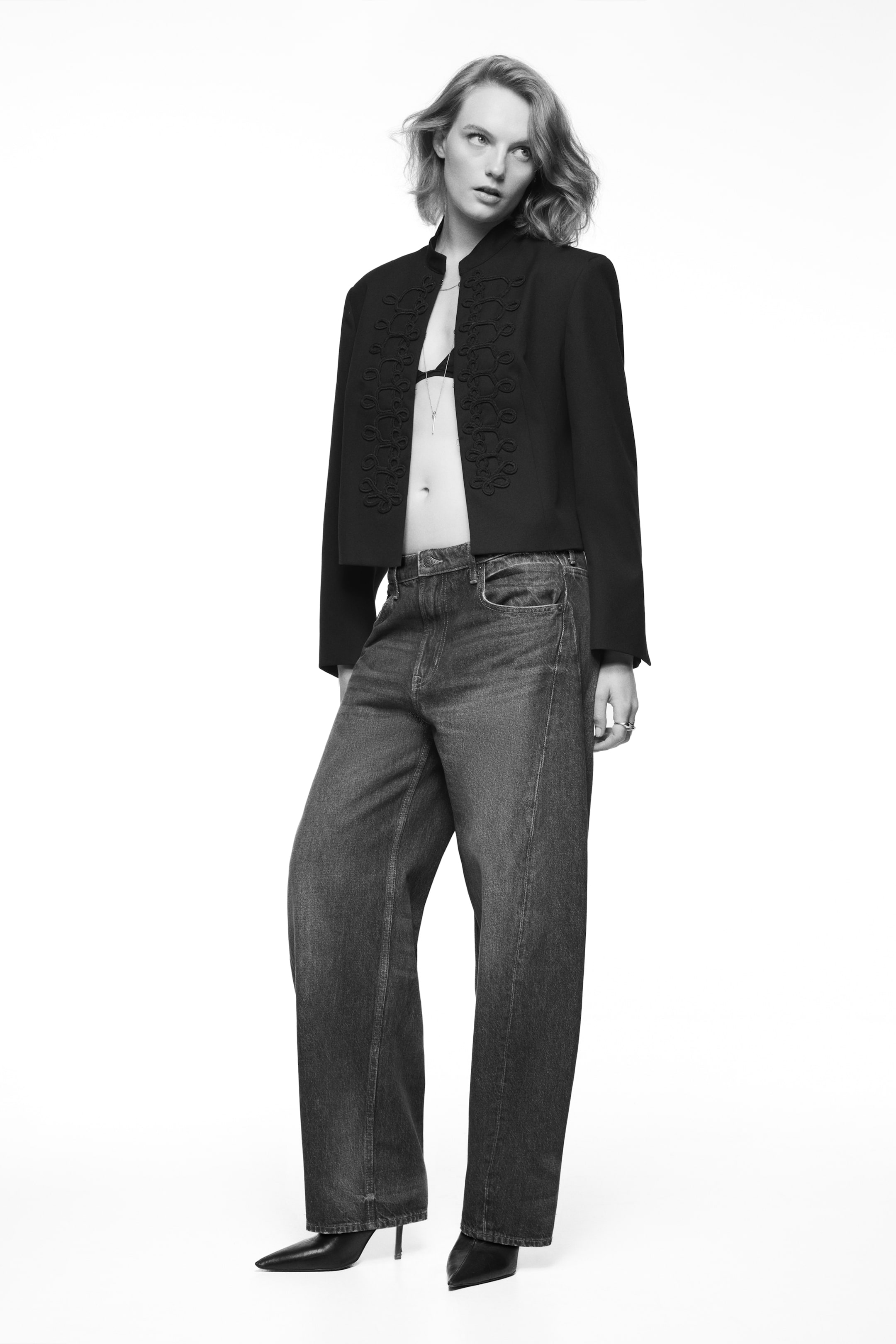 Büyük resmi görüntüle: Modelin üzerinde, koyu yıkamalı, normal bel kesimine ve kavisli, hacimli paçalara sahip beş cepli denim jean yer alıyor. Normal boydaki jean, kısa kesimli, işlemeli bir ceket ve sivri burunlu topuklu botlarla tamamlanmış.