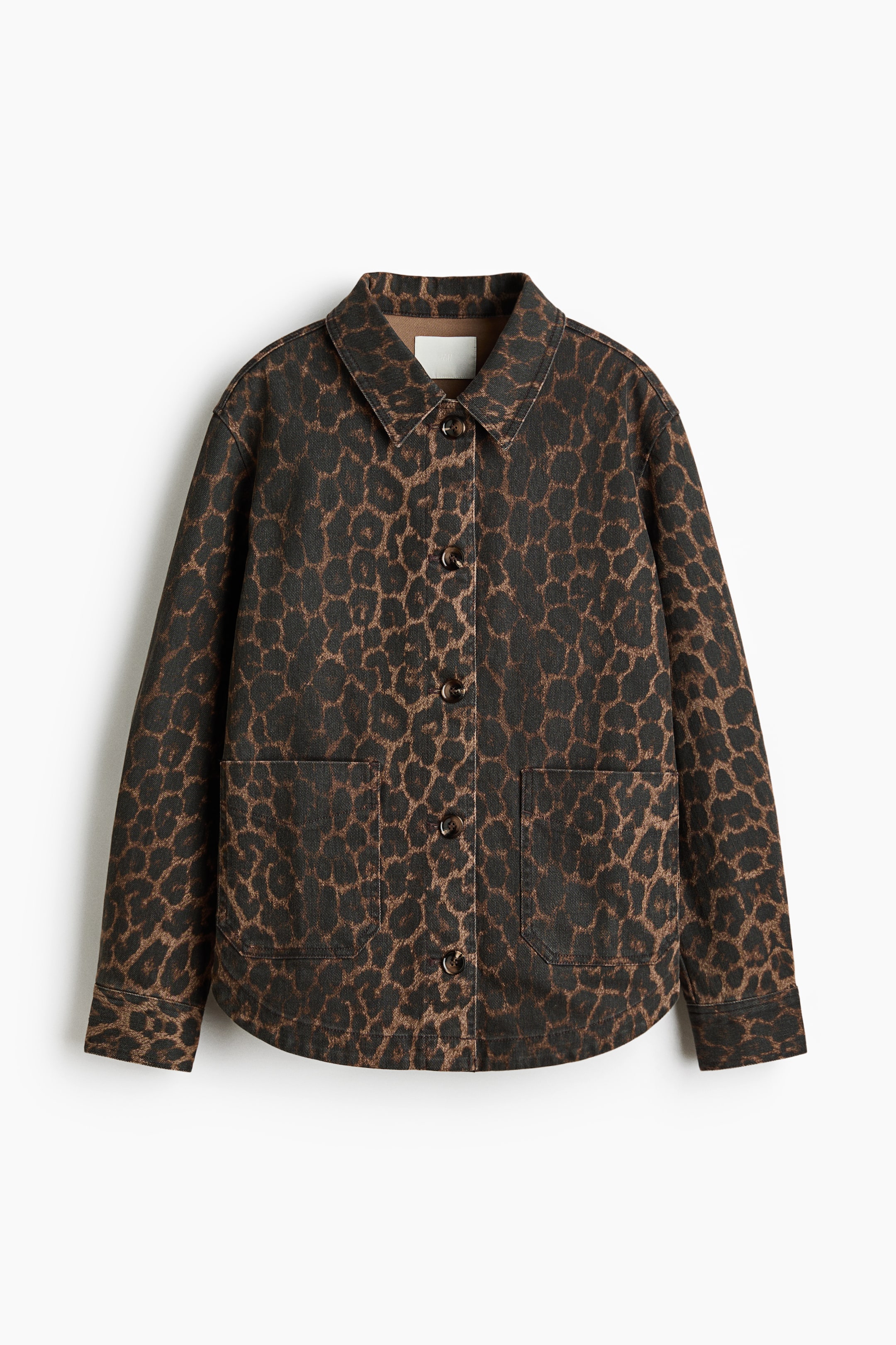 Ampliar la imagen: Una chaqueta de mezcla entre camisa y chaqueta en sarga de algodón presenta su PARTE FRONTAL, con un estampado de leopardo marrón y negro. Está diseñada con un cuello, botones en la parte delantera, dos bolsillos delanteros con solapa, hombros caídos, mangas largas con puños abotonados, y un dobladillo recto con aberturas laterales redondeadas.