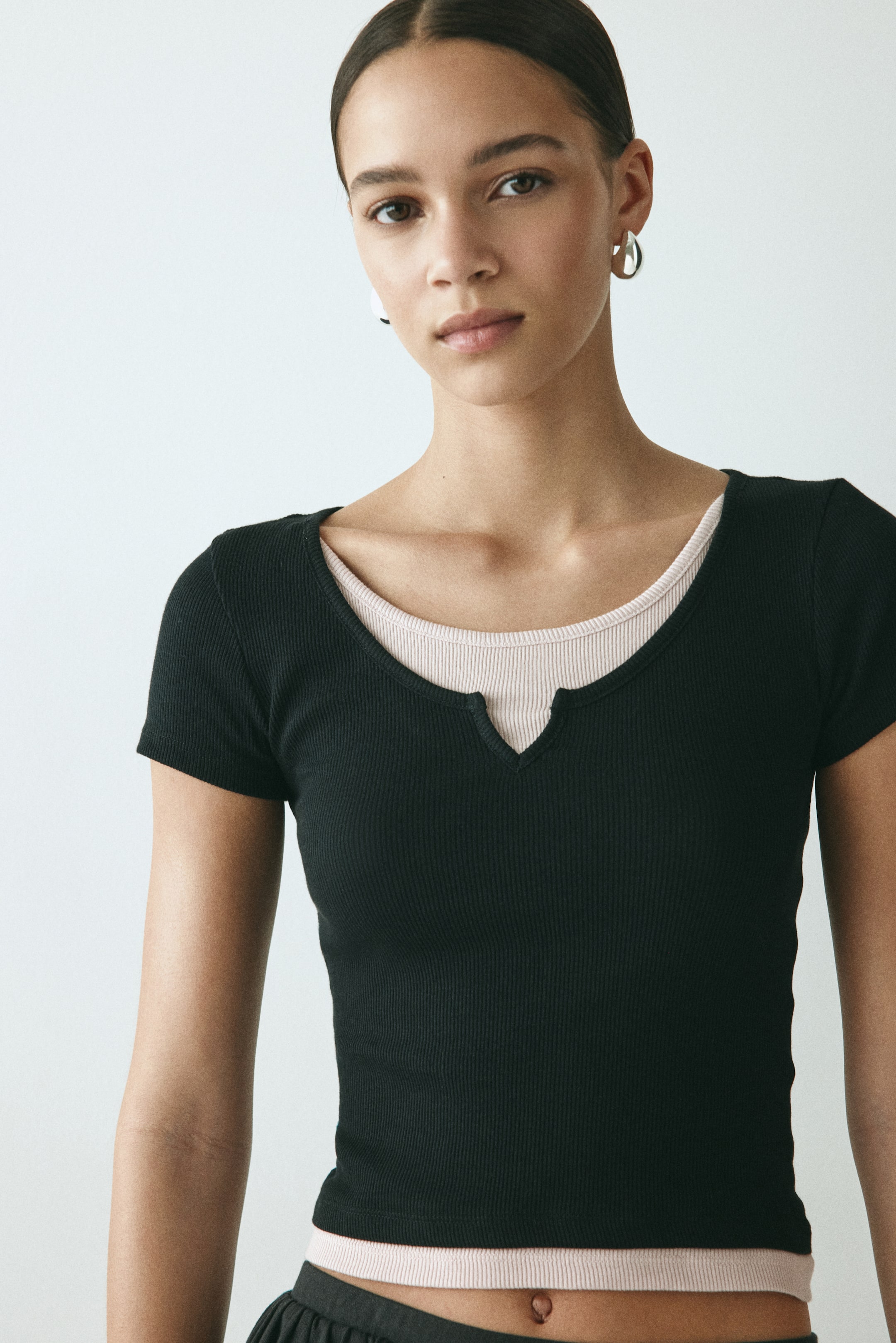 查看大圖: 黑色羅紋短袖上衣，採用缺口V領設計。與一件淺粉紅羅紋上衣疊穿，內層的圓領與下擺從下方露出。