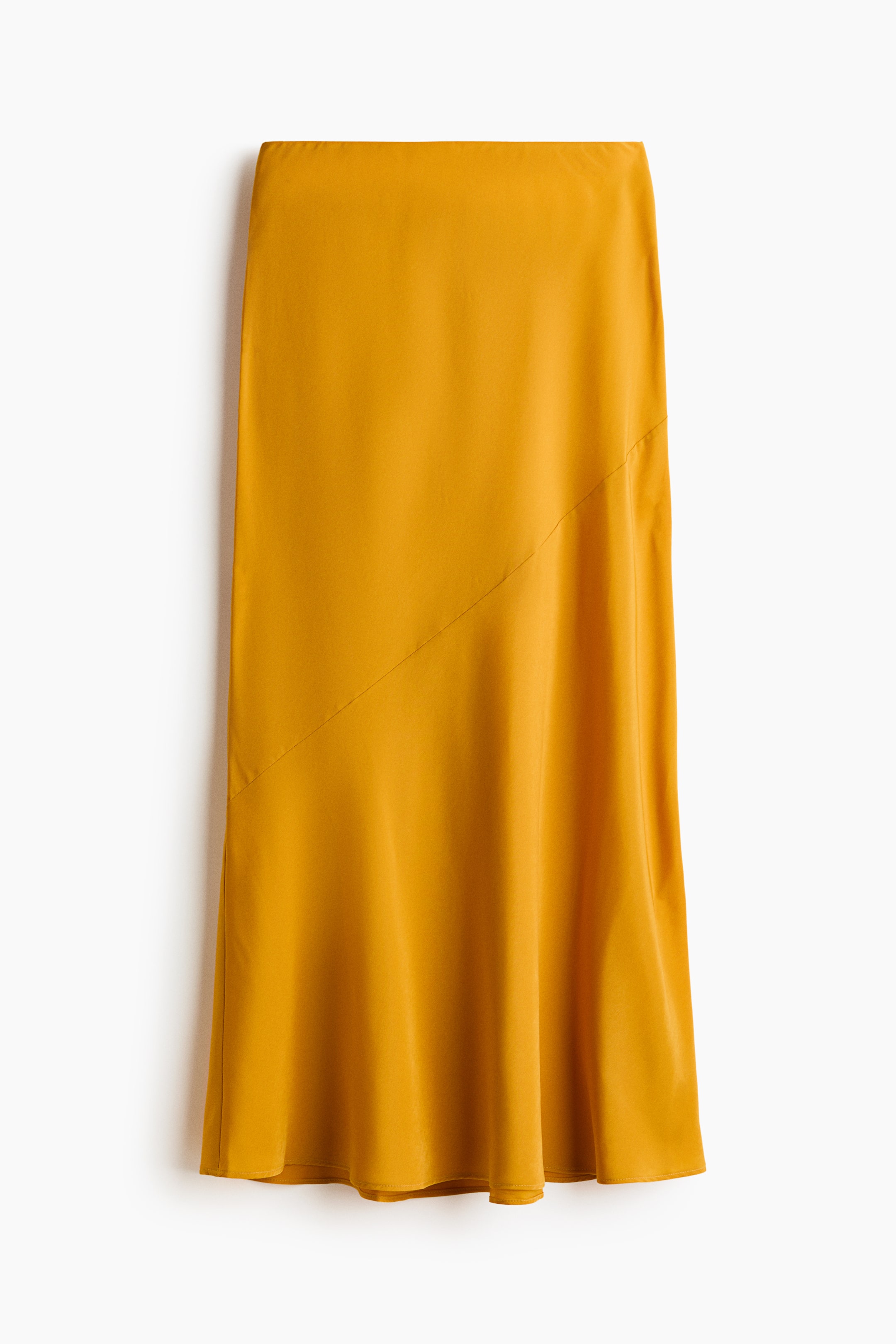 View larger image: A golden yellow midi skirt is displayed from the front, showcasing a flowing silhouette with a distinct diagonal seam on the upper left. The smooth fabric drapes softly, creating gentle folds towards the hem.