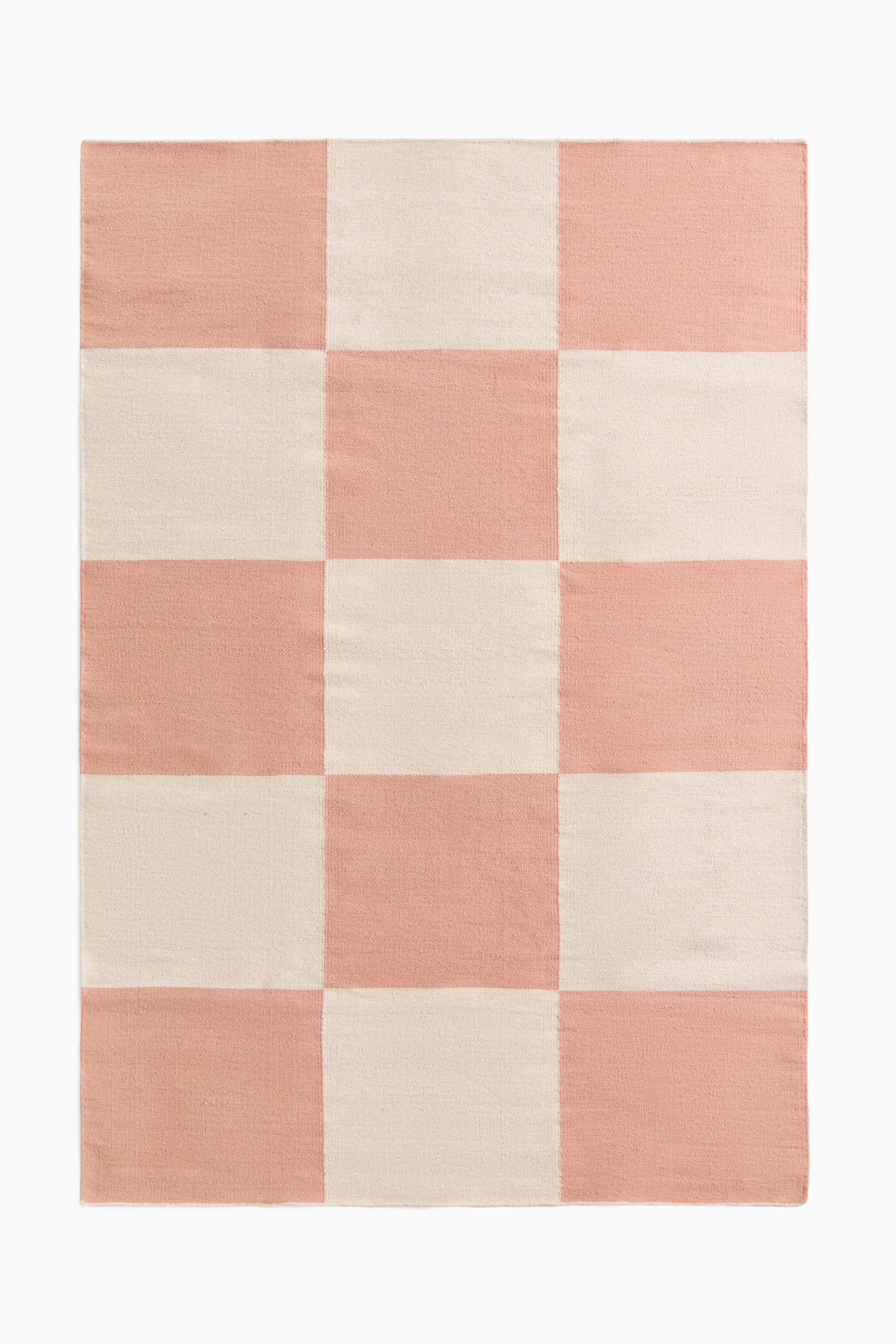 Agrandir l'image: Un tapis en coton tissé présente un grand motif à carreaux, avec une alternance de carrés rose et blanc cassé.