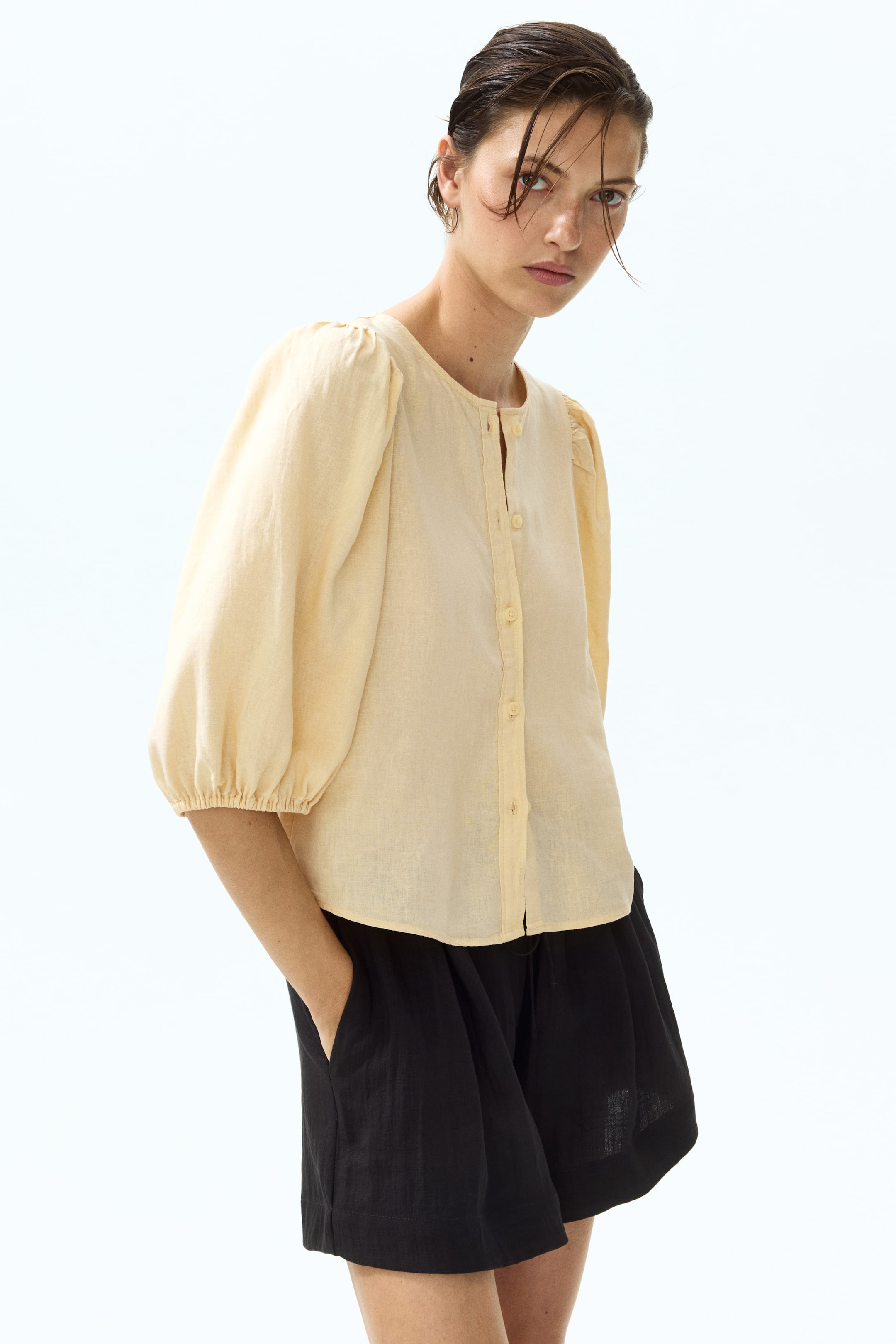 View larger image: The model is wearing a fitted, pale yellow blouse crafted from a breezy linen blend. It showcases a round neckline, buttons down the front, and 3/4-length balloon sleeves with elasticated cuffs.