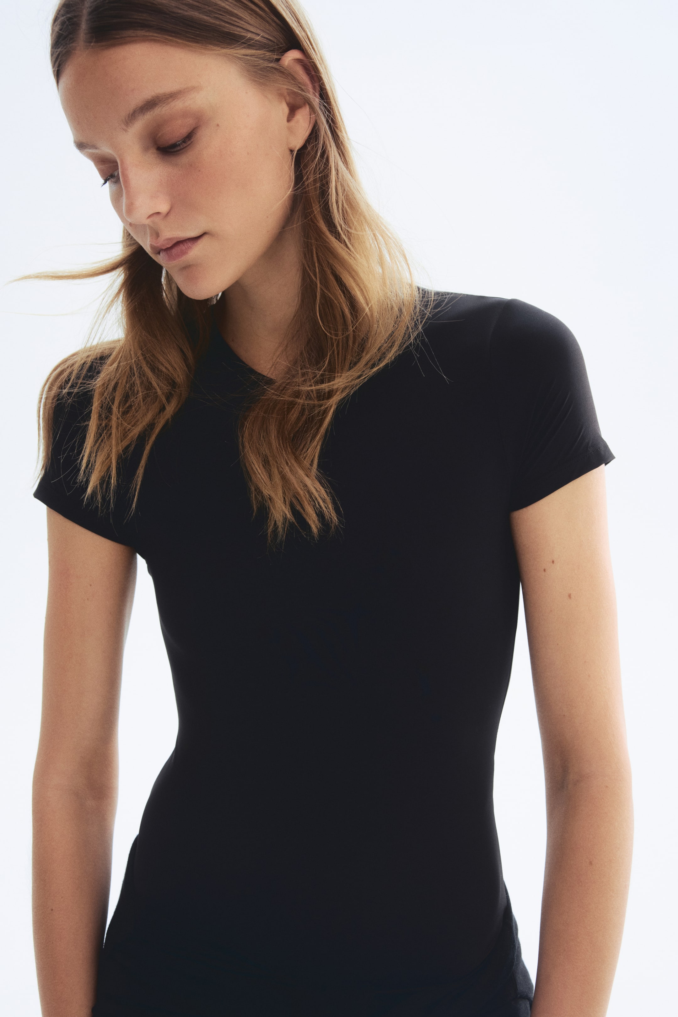 Agrandir l'image: Un haut noir à manches courtes avec un col rond et des manches ajustées. Il présente une silhouette lisse et moulante vue de face.