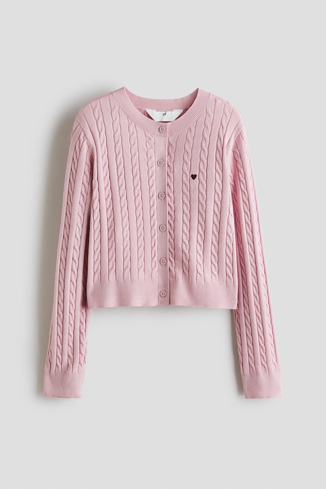 A pink cable knit cardigan is featuring a round, rib-trimmed neckline and buttons down the front. A small dark heart is embroidered on the chest, and it has long sleeves with ribbed cuffs and a ribbed hem. - 1