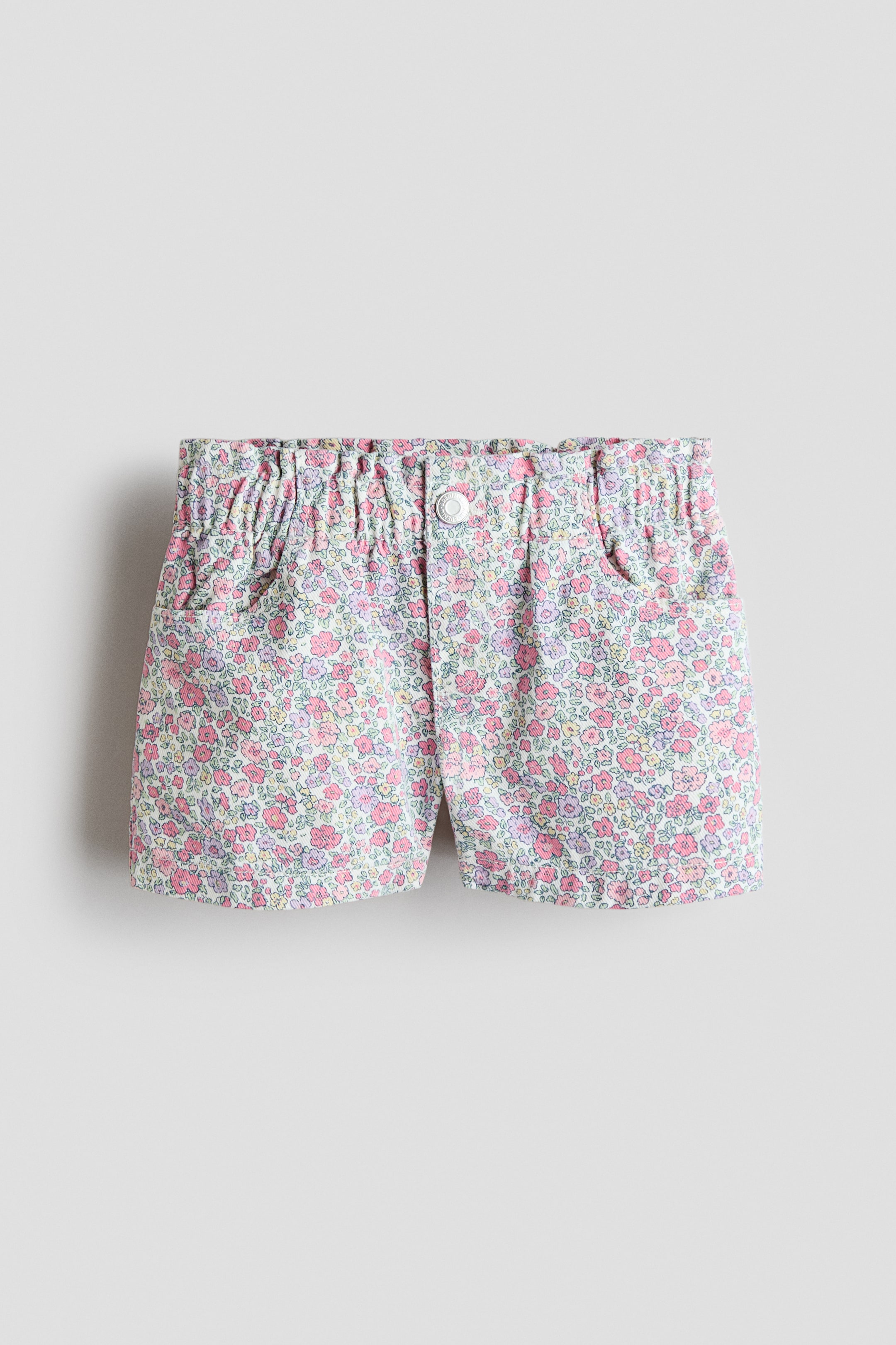 View larger image: Loose-fit shorts in washed cotton denim showcasing a floral pattern in shades of pink, purple, and green, as seen from the front. They boast an elasticated, gathered paper bag waist, a faux fly with a white press-stud, and diagonal front pockets.