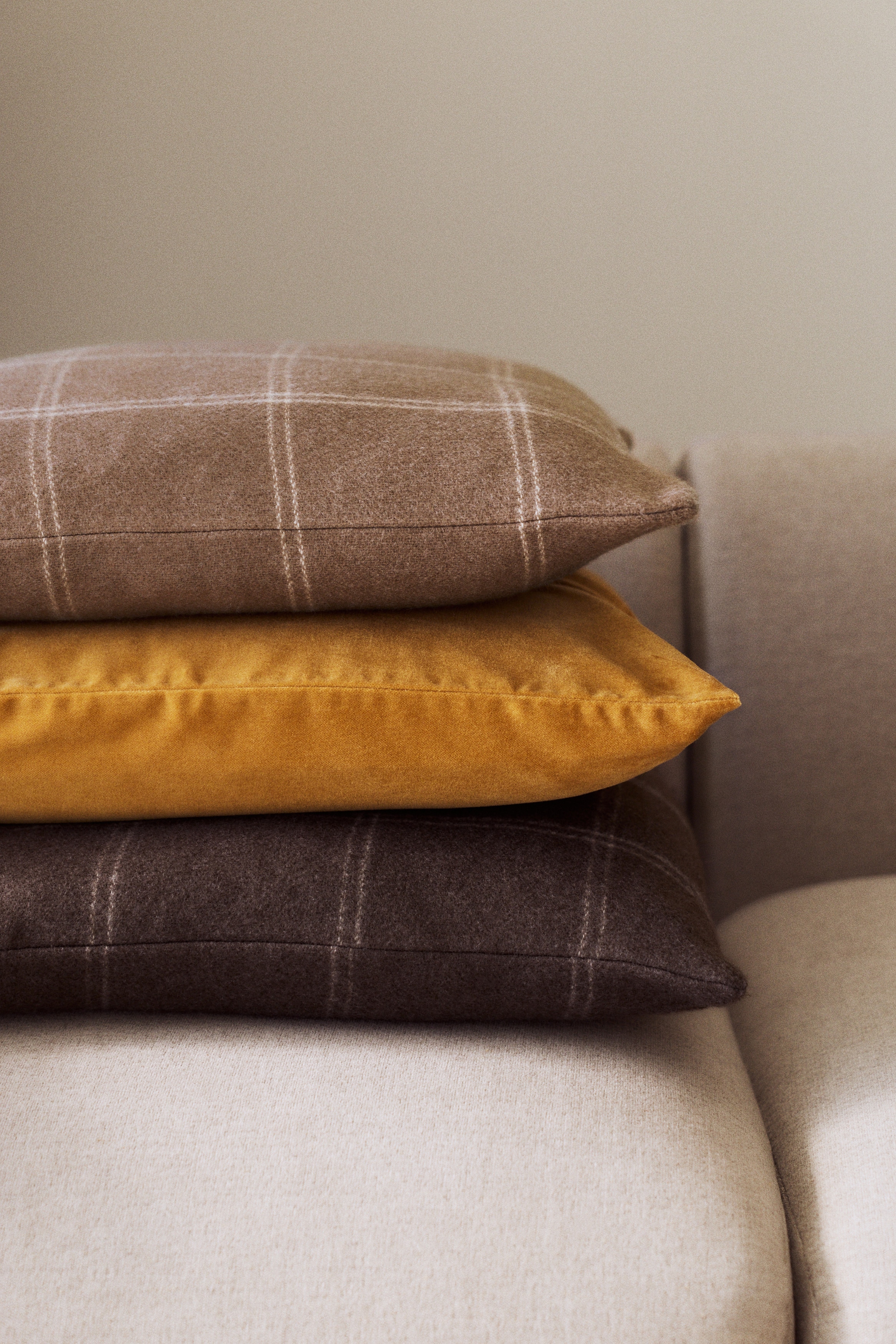 A square pillow showcases a brown fabric adorned with a light beige plaid pattern, featuring intersecting thin and slightly thicker lines.
