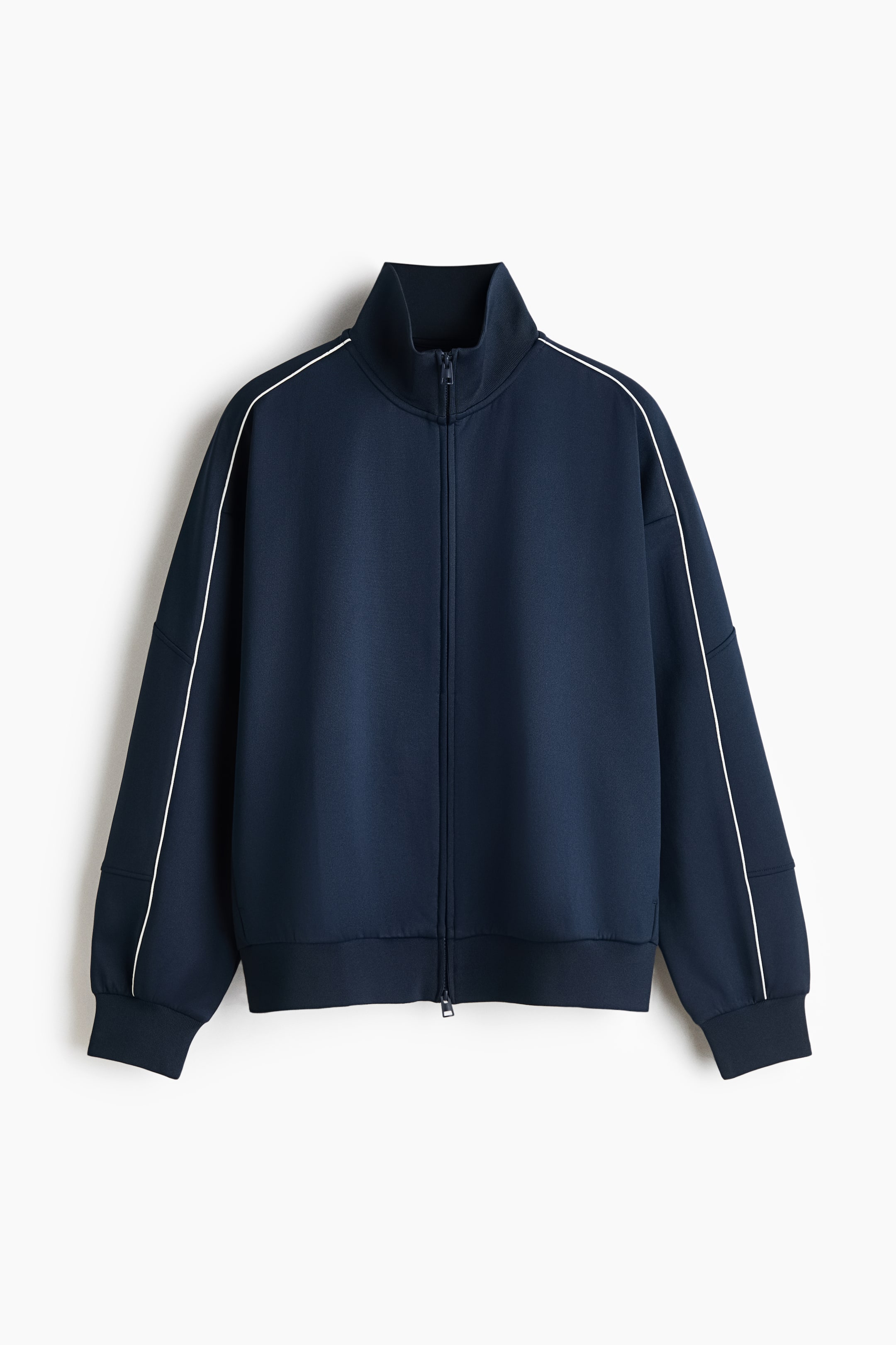 View larger image: A navy blue zip-up track jacket is shown from the front, featuring a high stand-up collar and a relaxed fit with dropped shoulders. Thin white piping runs along the shoulders and down the sleeves, which are finished with ribbed cuffs and a matching ribbed hem.