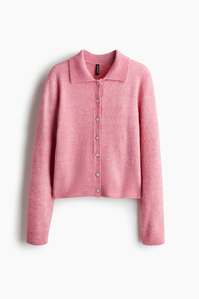 A pink knit cardigan is hanging, presenting its front view. It is featuring a pointed collar, a full front button closure with seven sparkling silver-toned buttons, and ribbed cuffs and hem. - 1