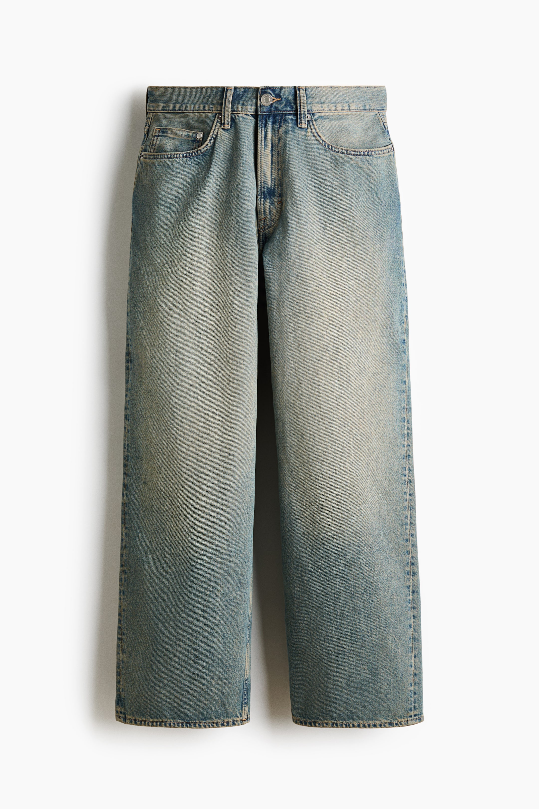 Grotere afbeelding bekijken: Een paar 5-pocket jeans wordt gepresenteerd met de voorkant naar voren, met een normale taille en een ritssluiting met knoop. De stijve katoenen denim toont een lichte tot middelblauwe wassing met vervaging op de dijen en een donkerdere tint naar de zoom toe, en is ontworpen met een verlaagde kruis en een baggy, afgeronde pasvorm van het been, die voldoende ruimte biedt van de zit tot de zoom.