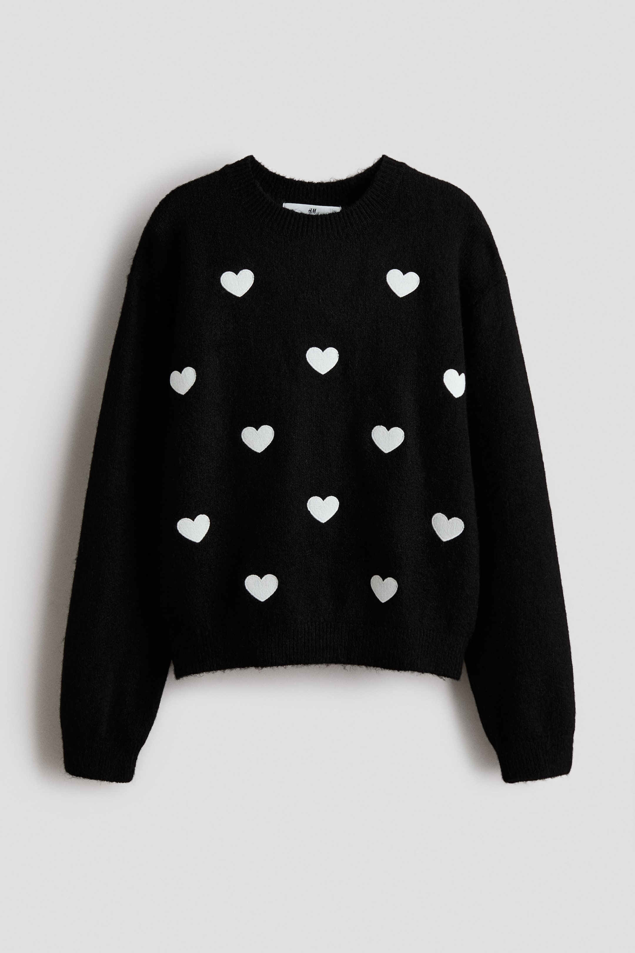 View larger image: A black jumper is displaying a soft, fine knit and scattered white hearts across its FRONT. 