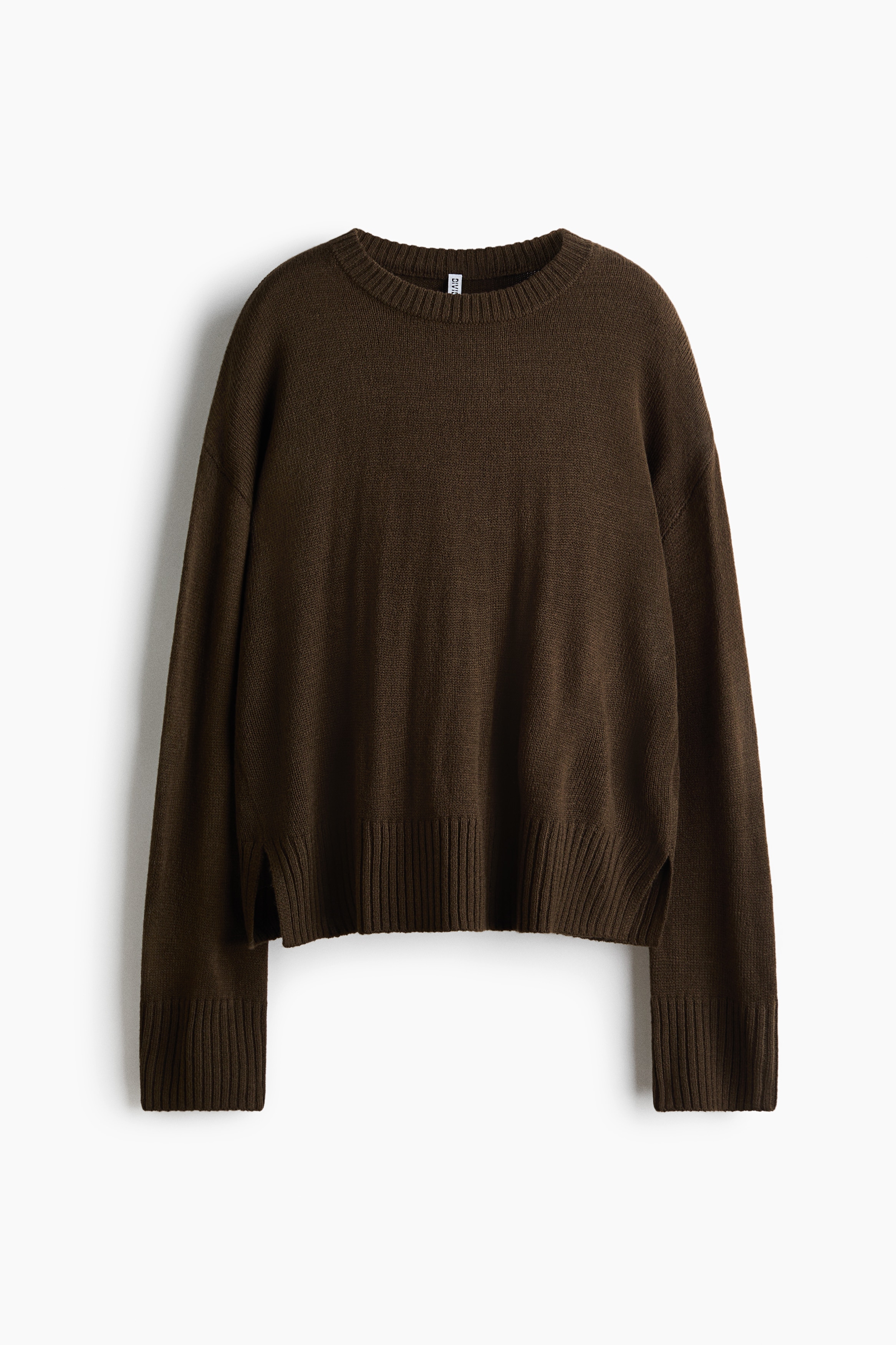 Een donker olijfgroene, losvallende trui in een zachte knit wordt gedragen door het model, met verlaagde schouders en lange mouwen met ribboorden. De trui, met een geribde zoom en zijsplit, wordt gecombineerd met olijfgroene wijde broekspijpen.