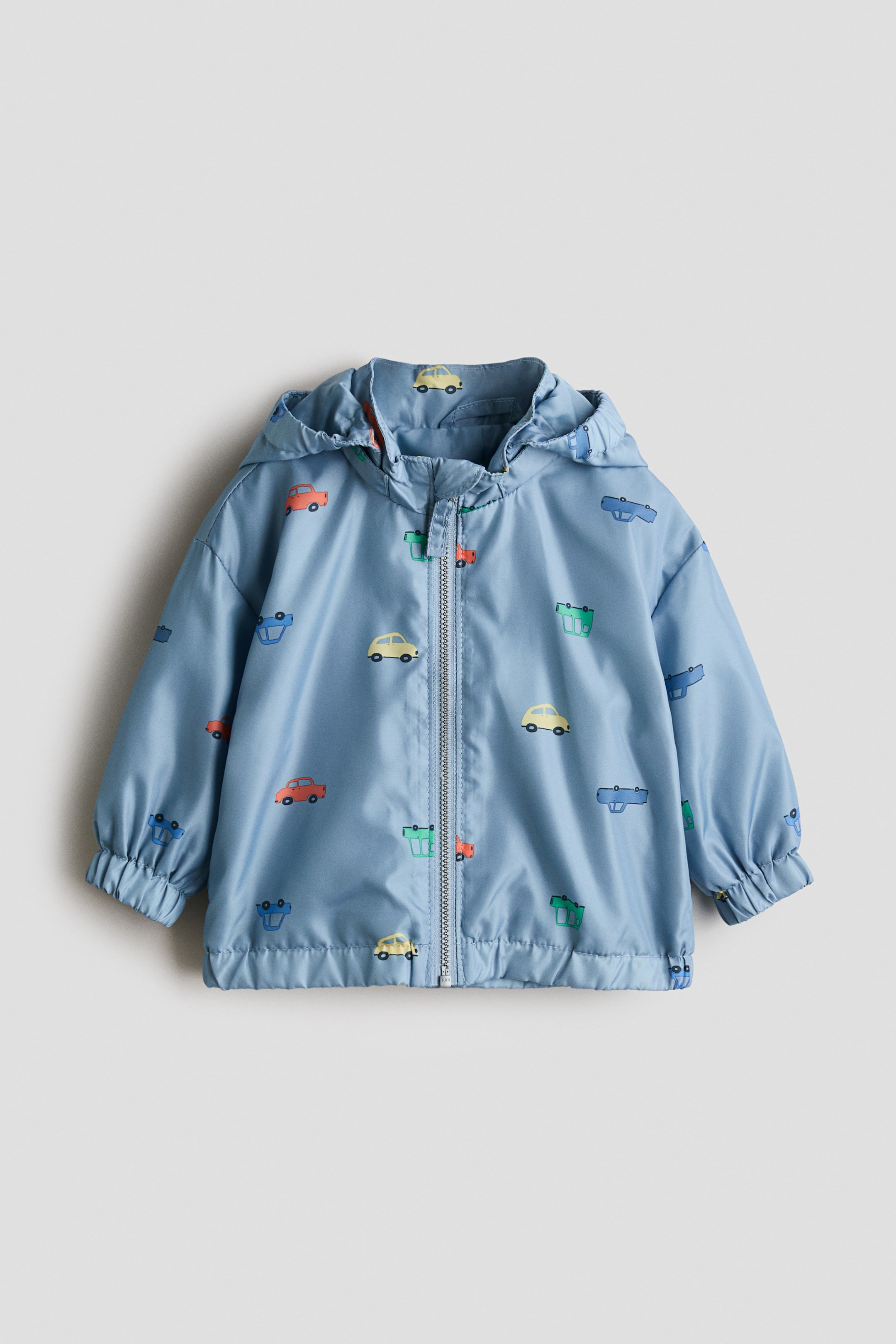 View larger image: A light blue jacket with a colourful car print is presented as FRONT, featuring a lined, detachable hood with covered elastication and a stand-up collar. It also showcases a front zip closure with an anti-chafe chin guard, dropped shoulders, and covered elastication at the cuffs and hem.