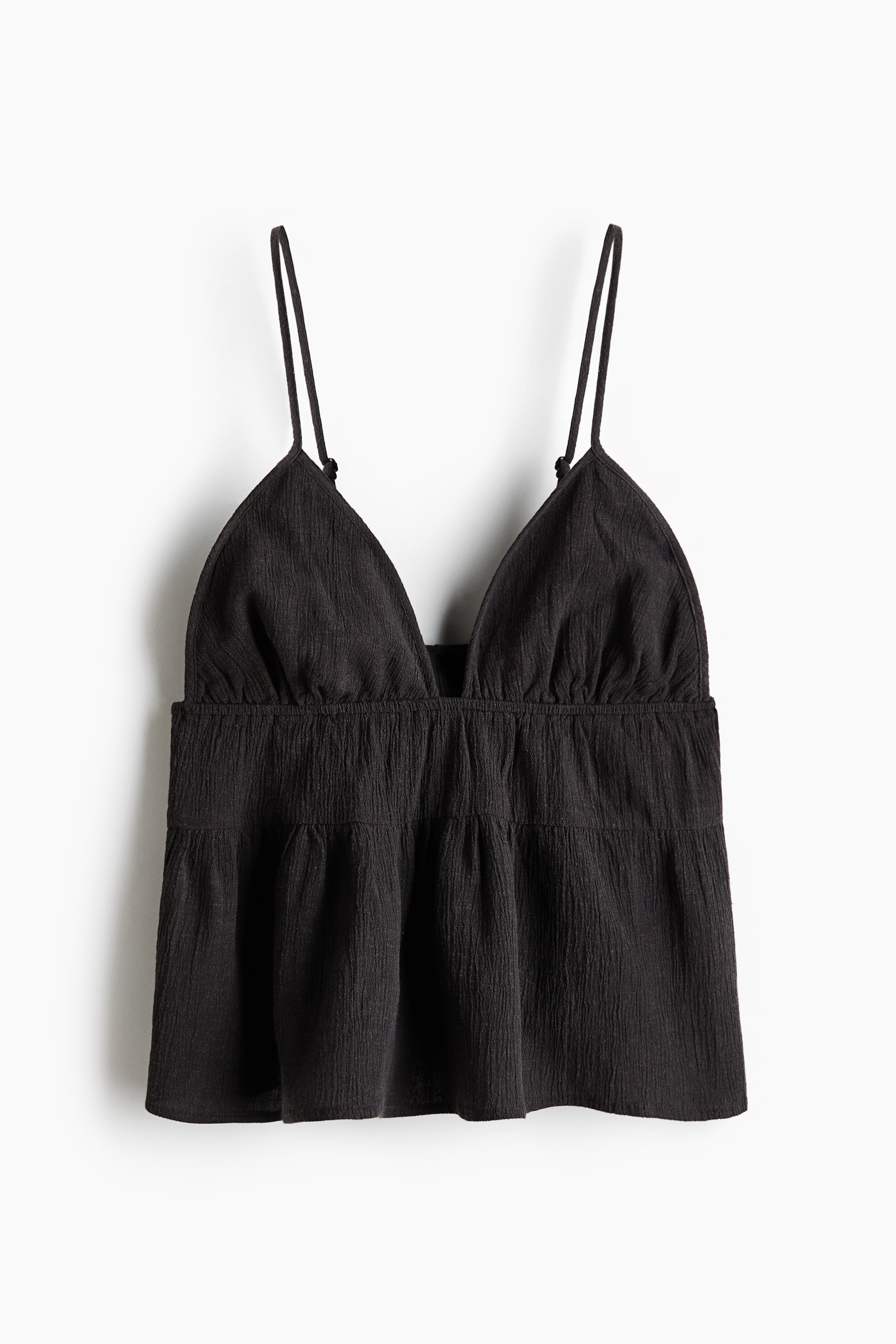 View larger image: A black camisole top is front-facing, featuring thin spaghetti straps and a deep V-neckline. It is designed with triangular bust cups above a gathered empire waist, which leads to a flowing, tiered peplum hem, all in a textured fabric.