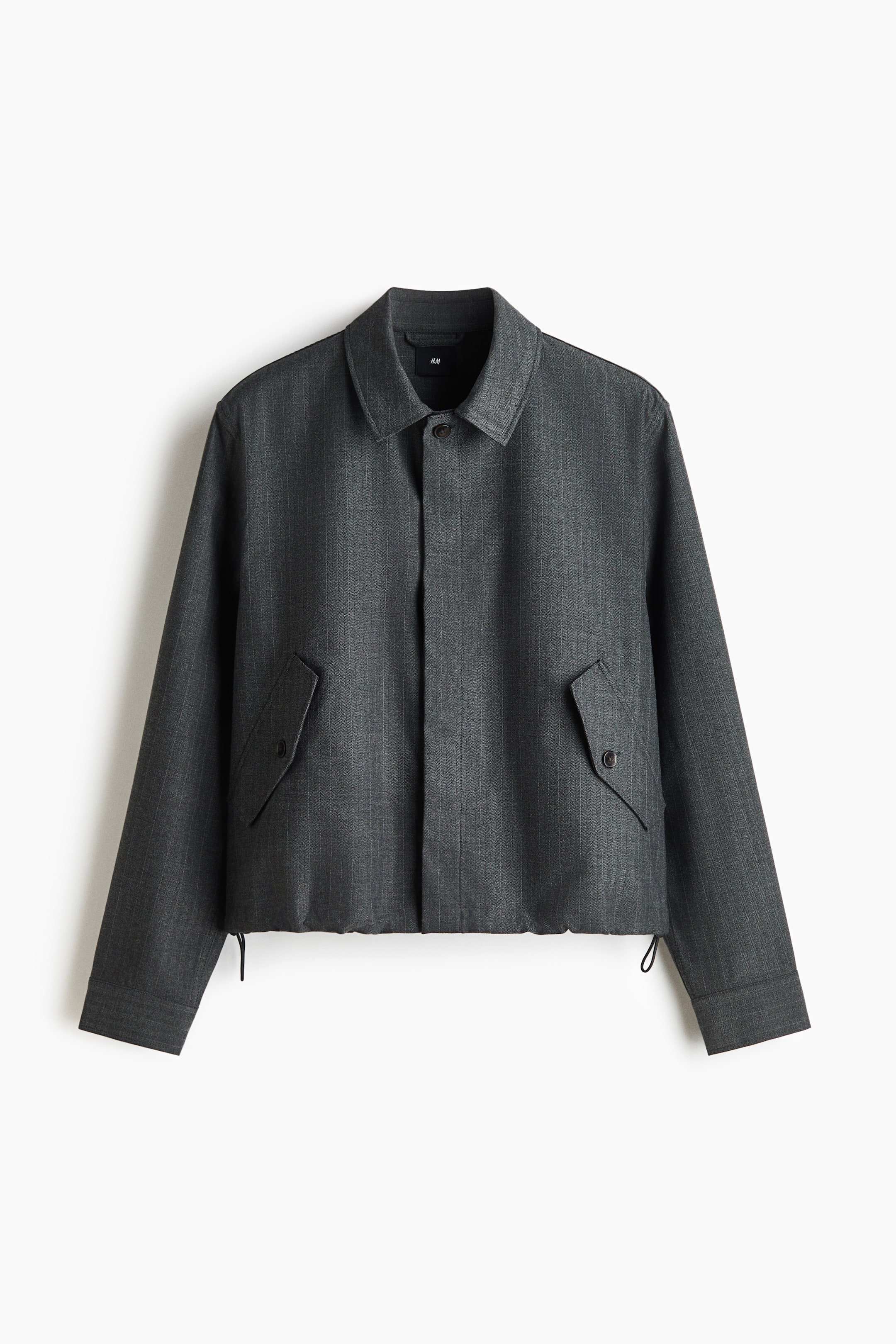 View larger image: A dark grey pinstriped jacket is shown from the front, featuring a point collar, concealed front placket, and two angled flap pockets with button closures. The jacket also features adjustable drawstring cords hanging from the hemline.