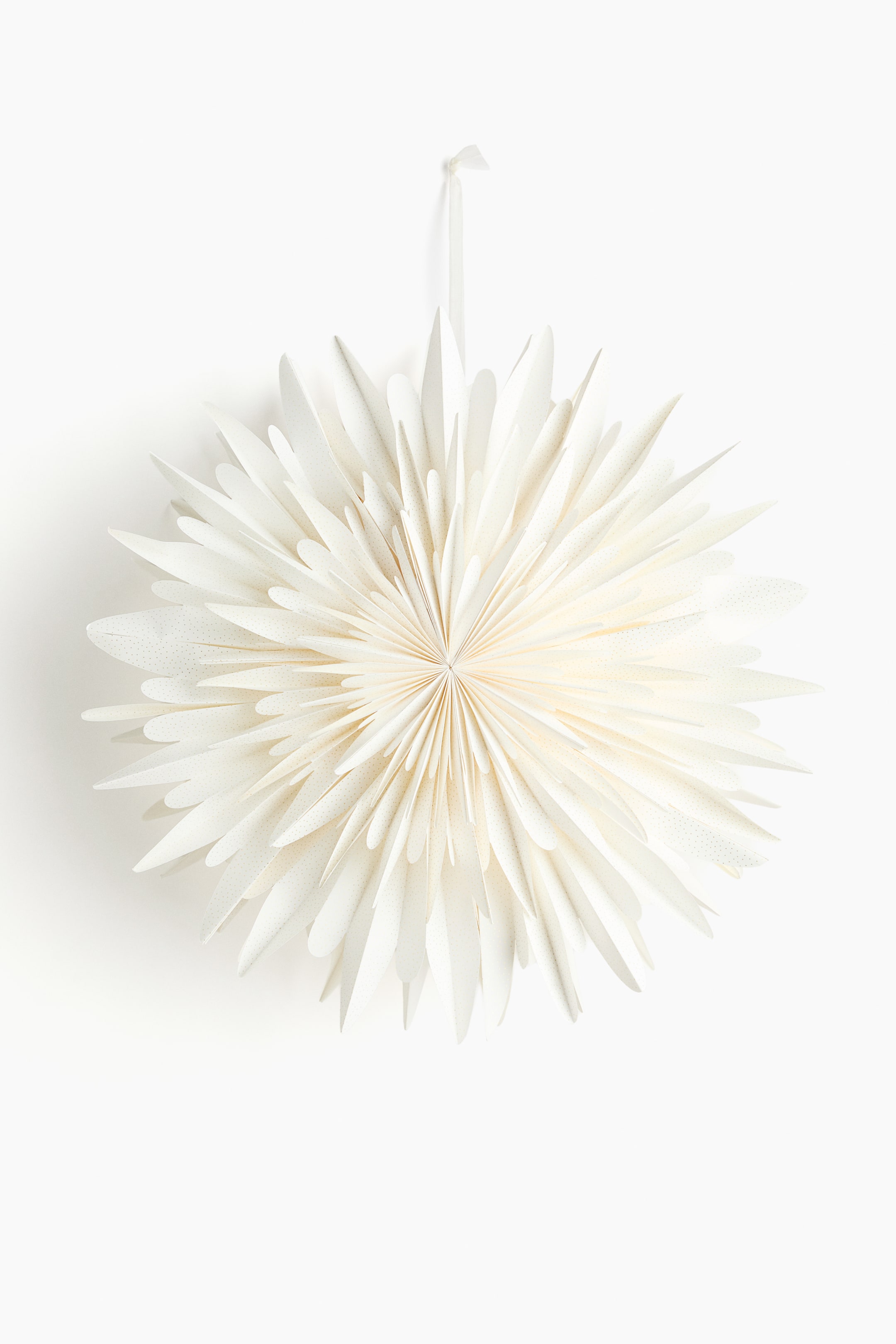 Se større billede: En papirstjerne præsenteres fra FORSIDEN, og viser en plisseret, lagdelt konstruktion, der minder om en fjerlet snefnug. Den har blødt afrundede kanter og en subtil plettet tekstur på dens off-white overflade, med et bånd fastgjort øverst til ophængning.