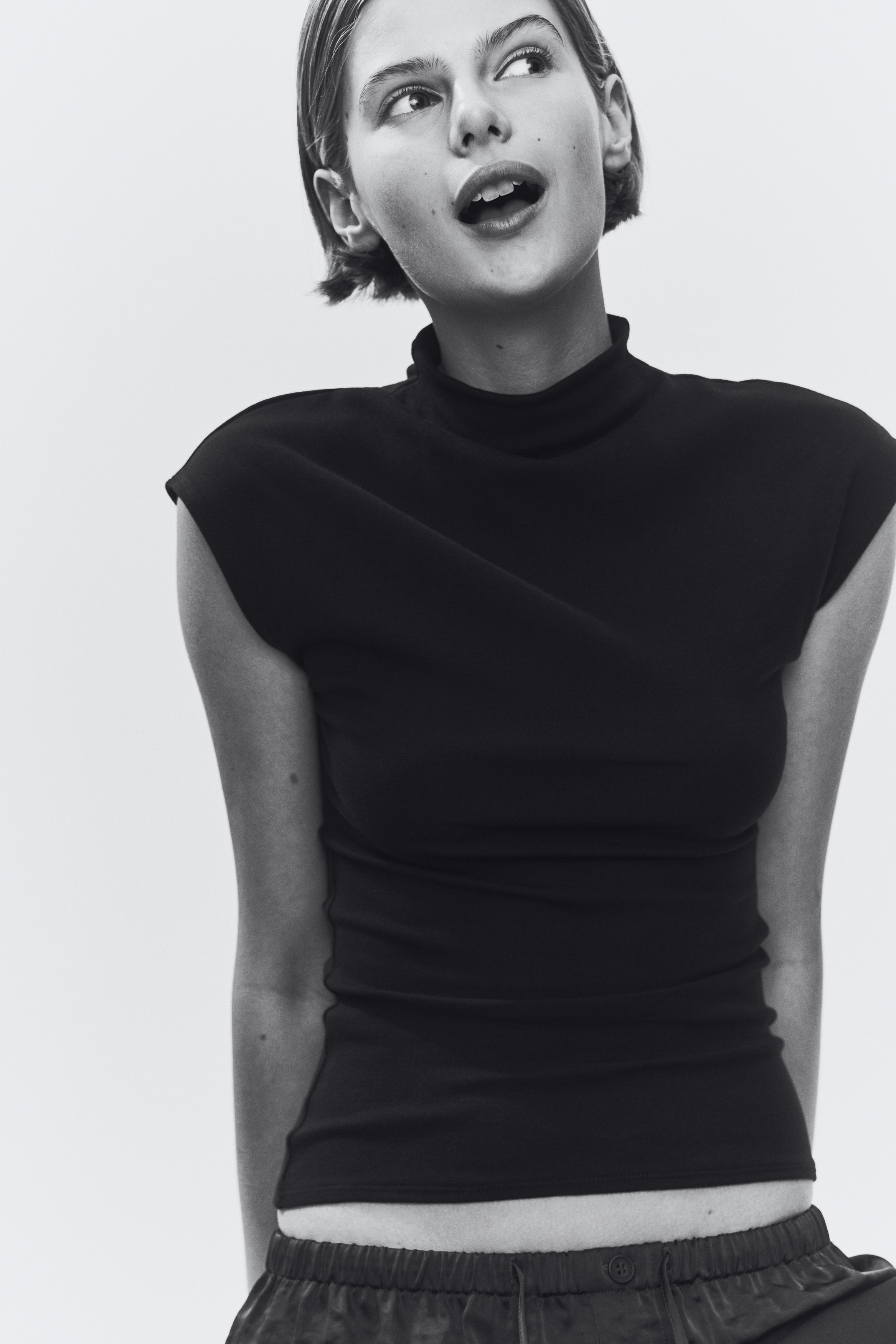 "A black top showcasing a mock neck and cap sleeves, presenting its front view. The garment exhibits a smooth texture with a straight hemline."